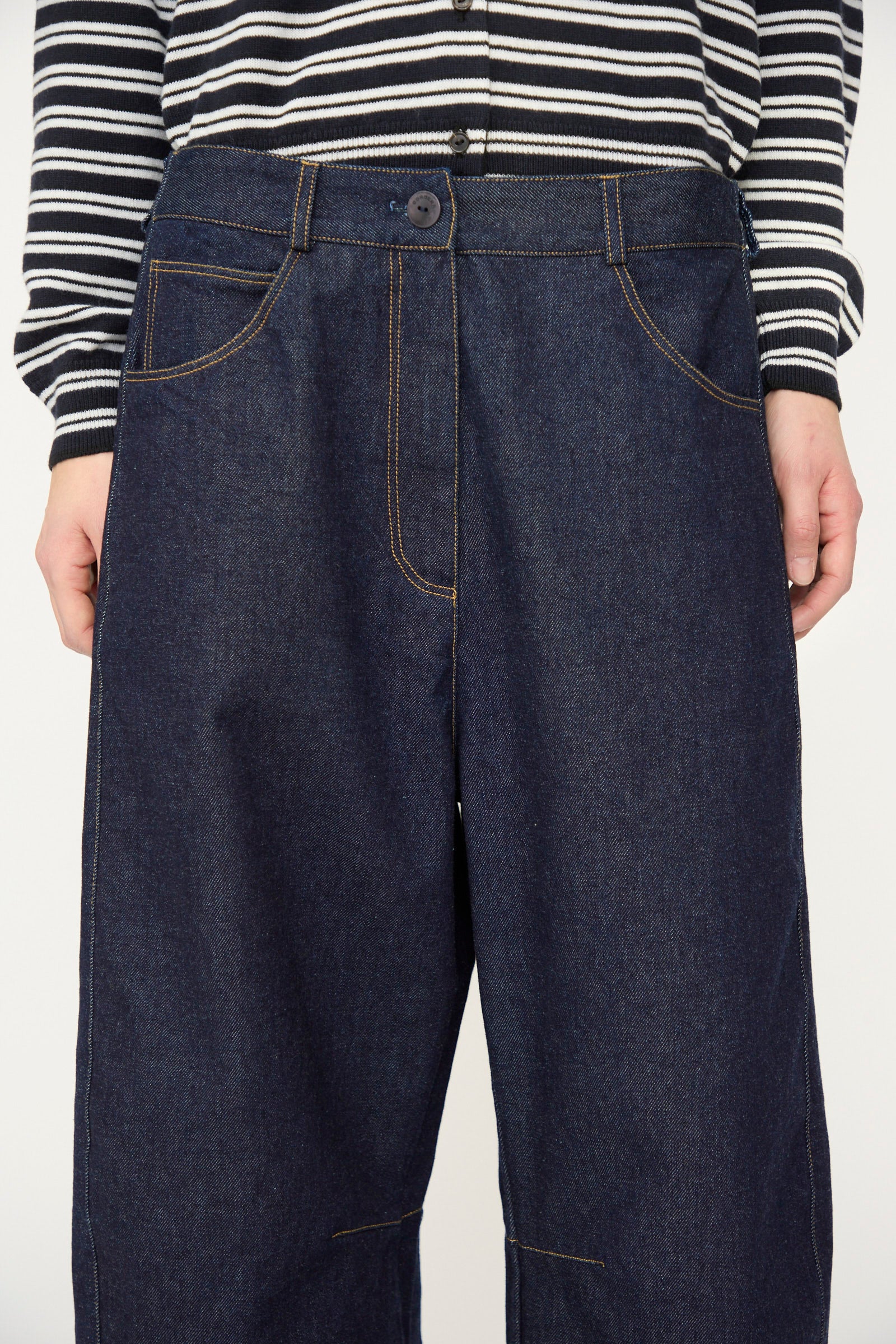 A person wearing a black and white striped long-sleeve shirt paired with Cordera's Curved Baggy Jean in Denim, featuring a high rise and visible brown stitching.