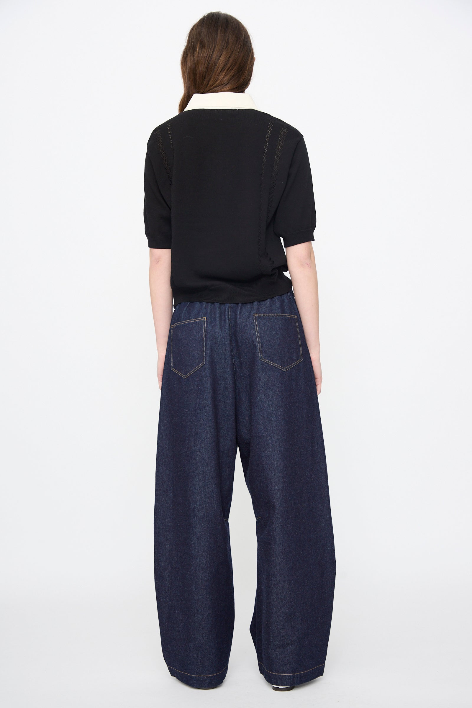 A person stands with their back to the camera, wearing a black short-sleeve shirt and Cordera Curved Baggy Jeans in denim, shown against a plain white background.