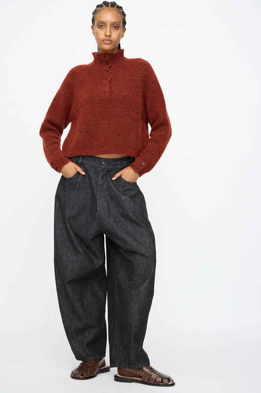 A person stands against a white background wearing a red knit sweater, Cordera Denim Baggy Pants in Black, and brown shoes, with hands in pockets.