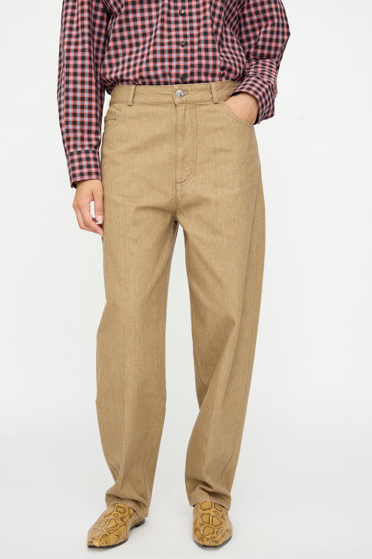 Cordera Denim Carrot Pants in Beige with a tapered leg, worn with a red and black plaid button-down shirt and snakeskin-patterned boots.