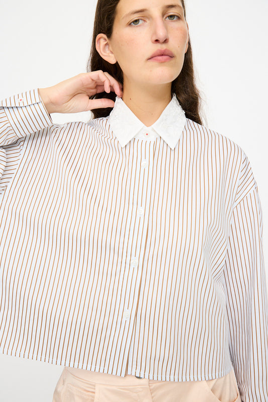 A person wearing Cordera's Embellished Shirt in Striped, featuring long sleeves, vertical brown stripes, and a white collar, poses with one hand touching their neck.