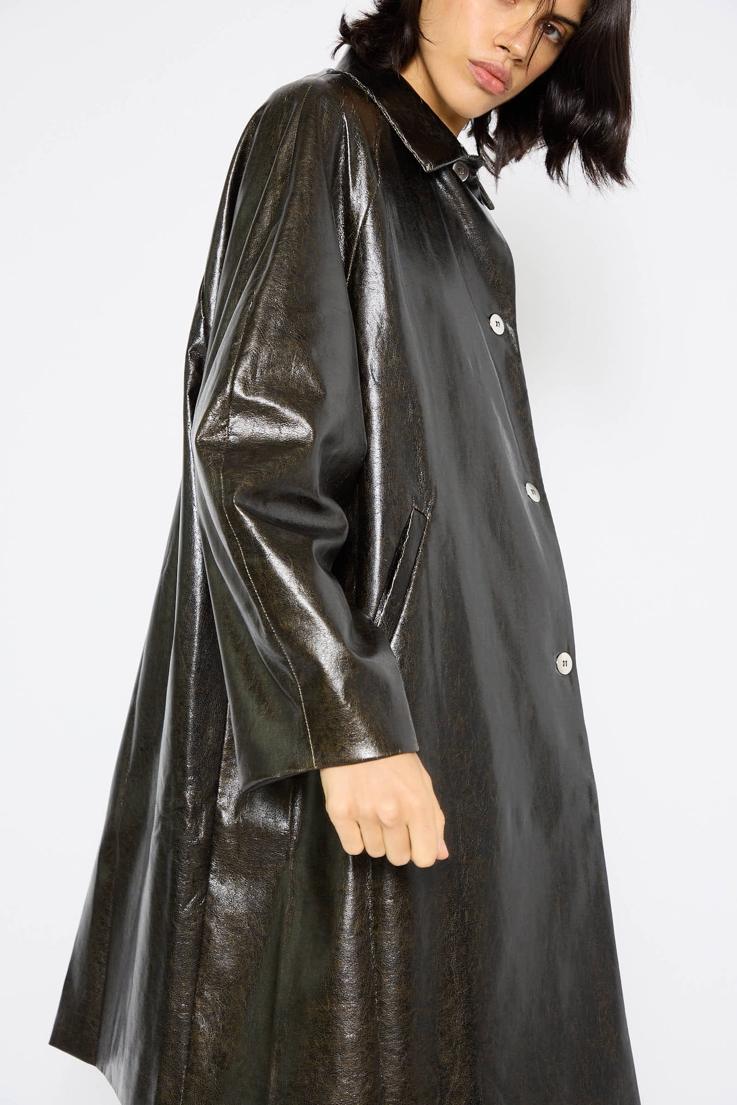 A person with short dark hair wearing a Cordera Faux Scratched Leather Coat in Black, featuring large buttons, poses against a plain background.