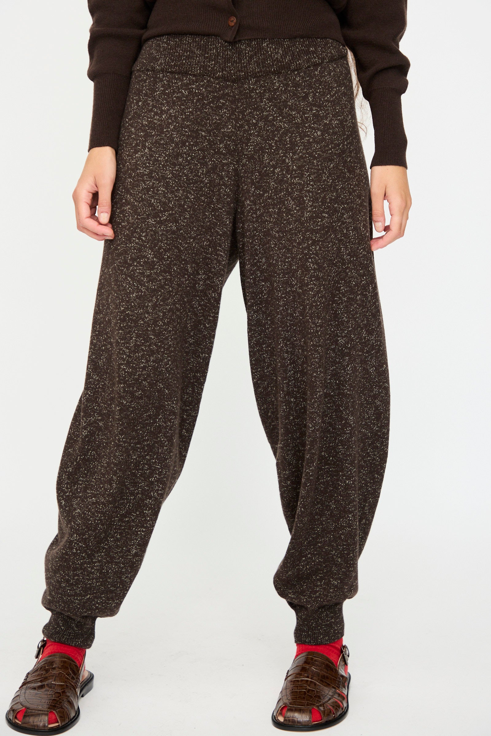 Person wearing Cordera's Flecked Cotton Pant in Brown, paired with a dark brown sweater, red socks, and brown sandals—standing against a plain white background.