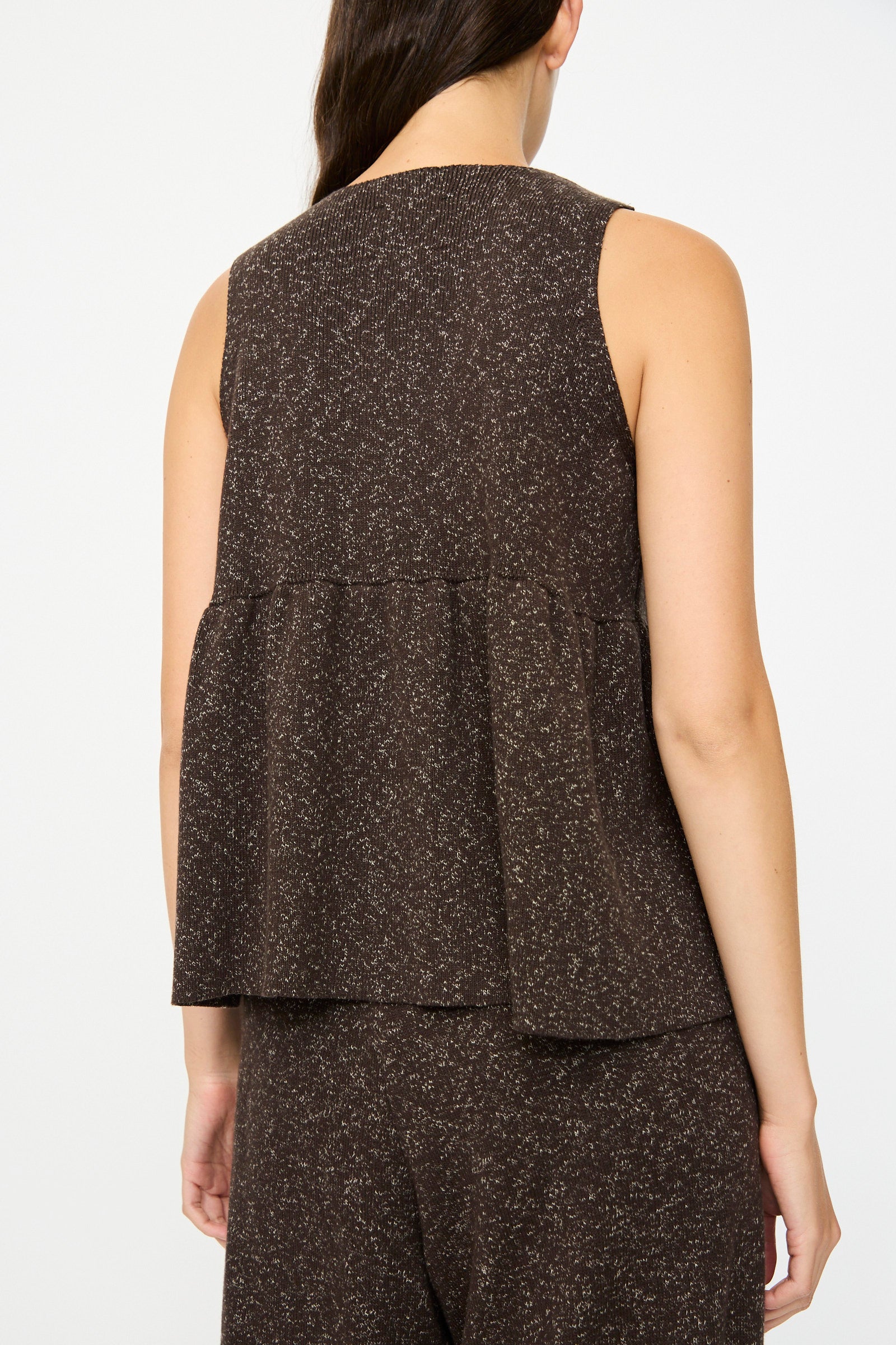 A woman is seen from the back wearing Cordera’s Flecked Cotton Peplum Top in brown, a sleeveless design with a loose, flared peplum silhouette, paired with matching pants.
