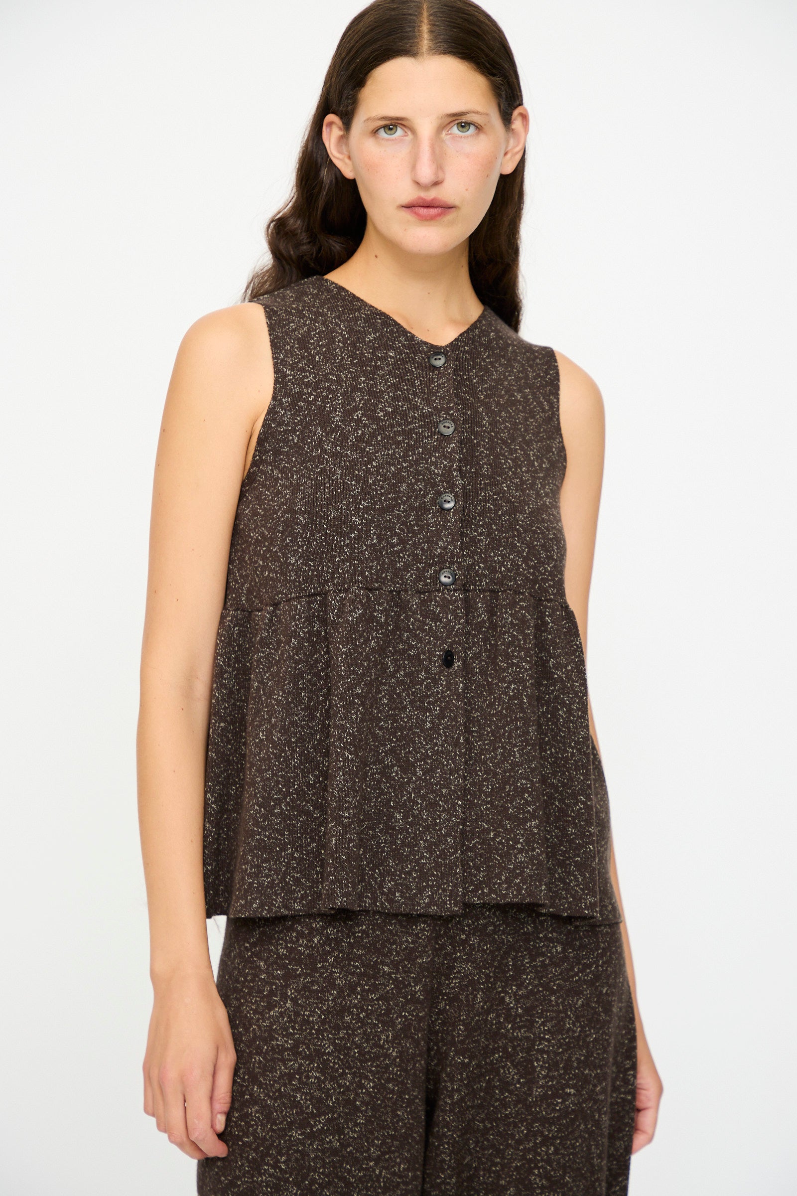 A woman with long brown hair wears the Cordera Flecked Cotton Peplum Top in Brown, styled with matching pants. She stands against a plain white background.