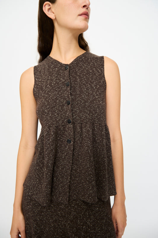 A woman wears the Flecked Cotton Peplum Top in Brown by Cordera, featuring a sleeveless design, textured button-front, and flared peplum silhouette, standing against a plain white background.