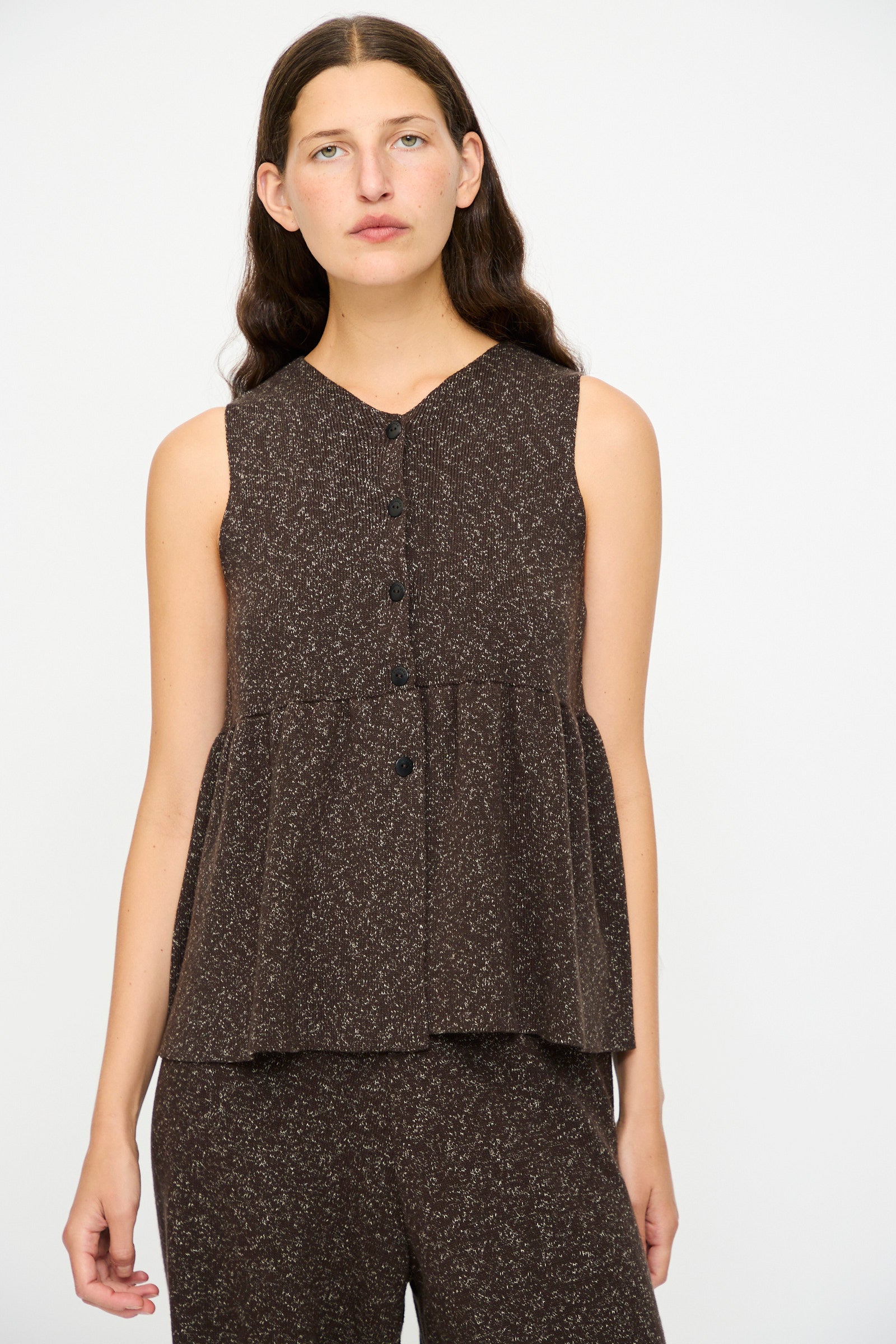 A woman with long brown hair wears the Cordera Flecked Cotton Peplum Top in Brown, paired with matching pants, standing against a plain white background.