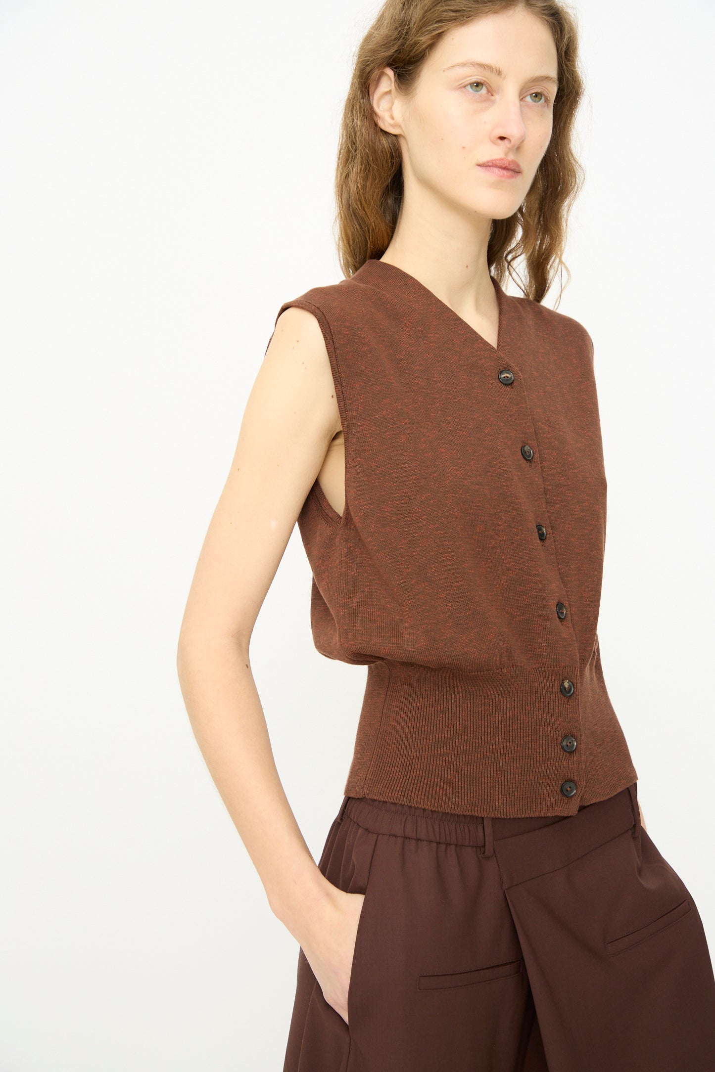 A person models Cordera’s Flecked Cotton Waistcoat in Russet with brown pants, both crafted from premium cotton in Spain, posed against a light plain background and gazing to the side.