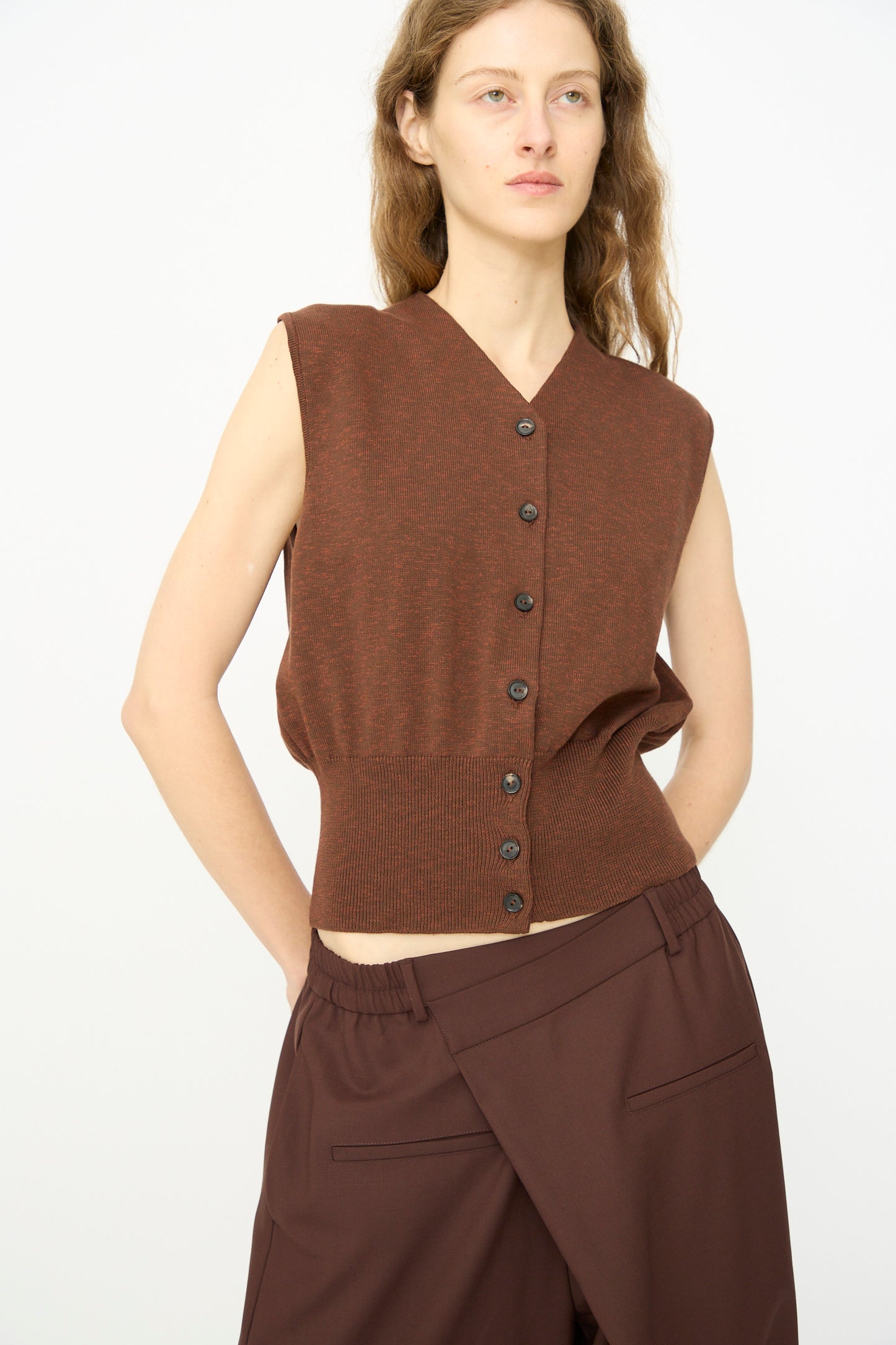 A person wears Cordera's Flecked Cotton Waistcoat in Russet with loose brown trousers, standing against a plain white background.