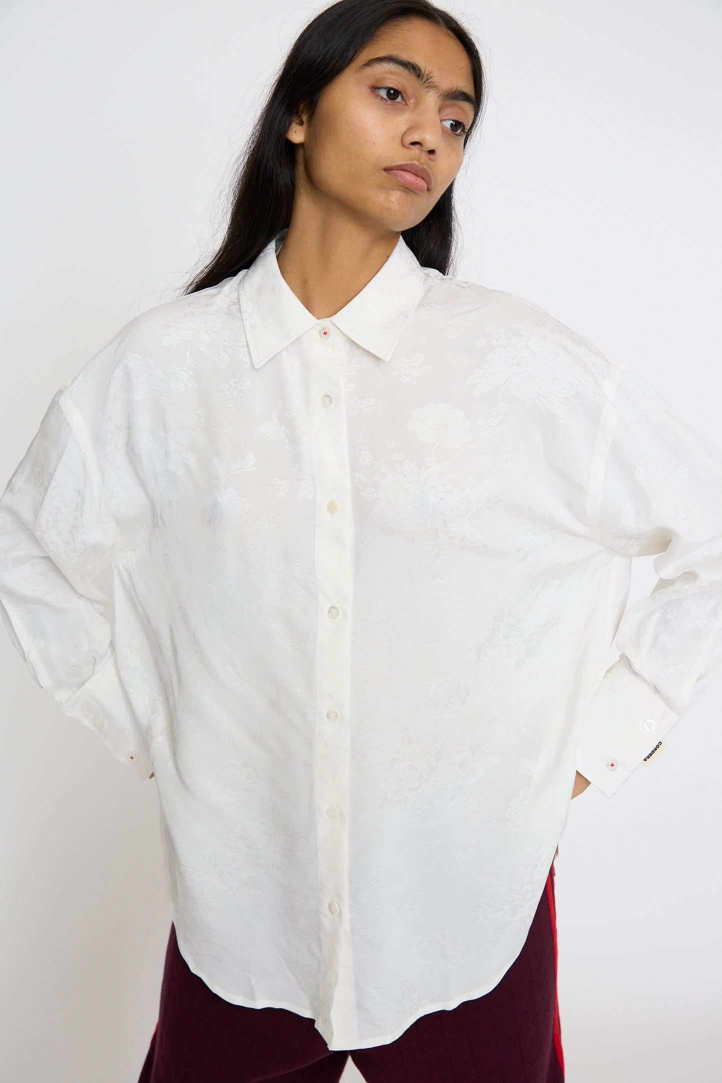 A person in Cordera's Flower Jacquard Shirt in White and red pants stands against a neutral background, looking to the side.