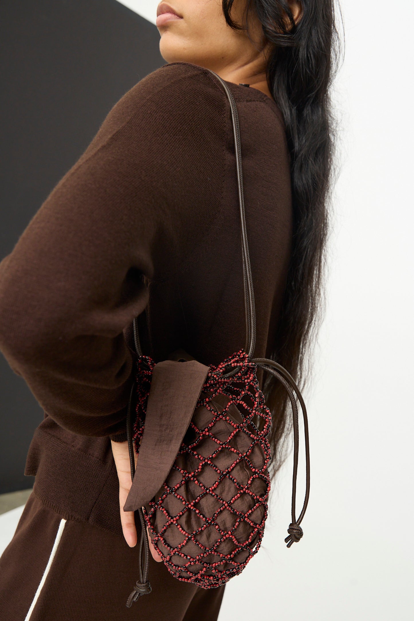A person wearing a brown outfit carries the Cordera Handmade Beaded Net Bag—featuring a red and brown beaded net design and handcrafted in Guatemala—over their shoulder.