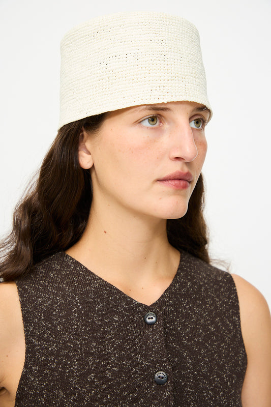 A woman with long brown hair wears a sleeveless dark brown textured top and the Cordera Handmade Fez Hat in Natural, looking slightly to the side.