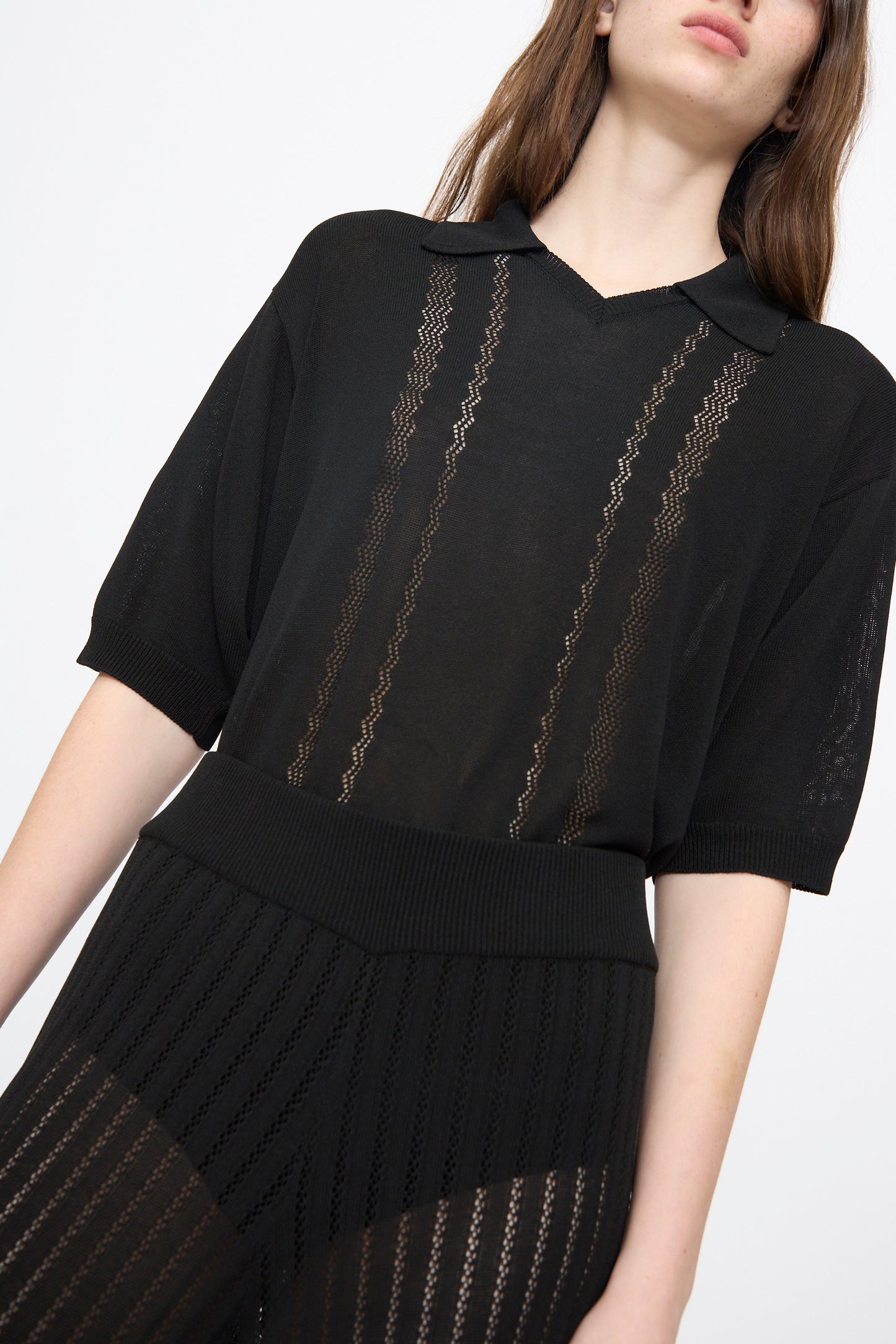 A woman wears Cordera’s Lace Knit Pants in Black with a matching short-sleeved top, both featuring zigzag patterns, as she stands against a plain white background.