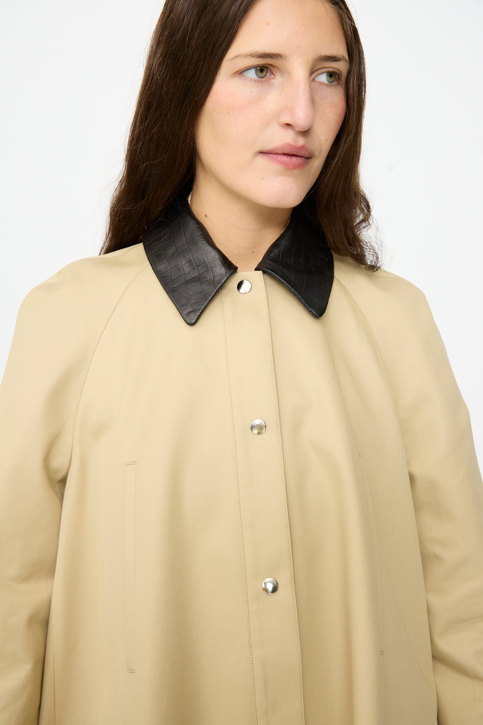 A woman models the Cordera Leather Collar Voluminous Coat in tan cotton, featuring silver buttons and a black lambskin leather collar, set against a plain white background.