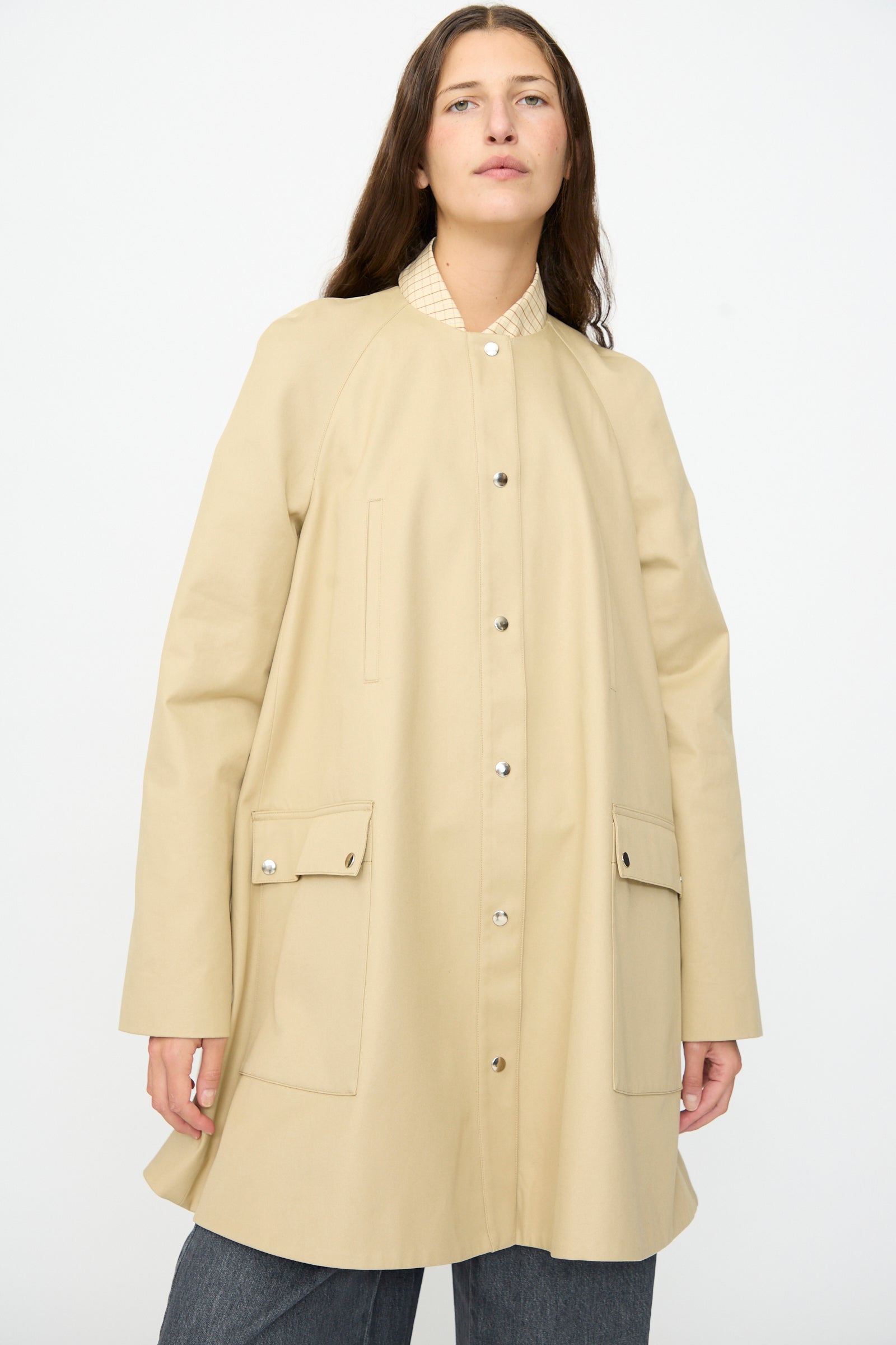 A woman models the Cordera Leather Collar Voluminous Coat, featuring a long beige A-line silhouette with large front pockets and a lambskin leather collar, standing against a plain white background.