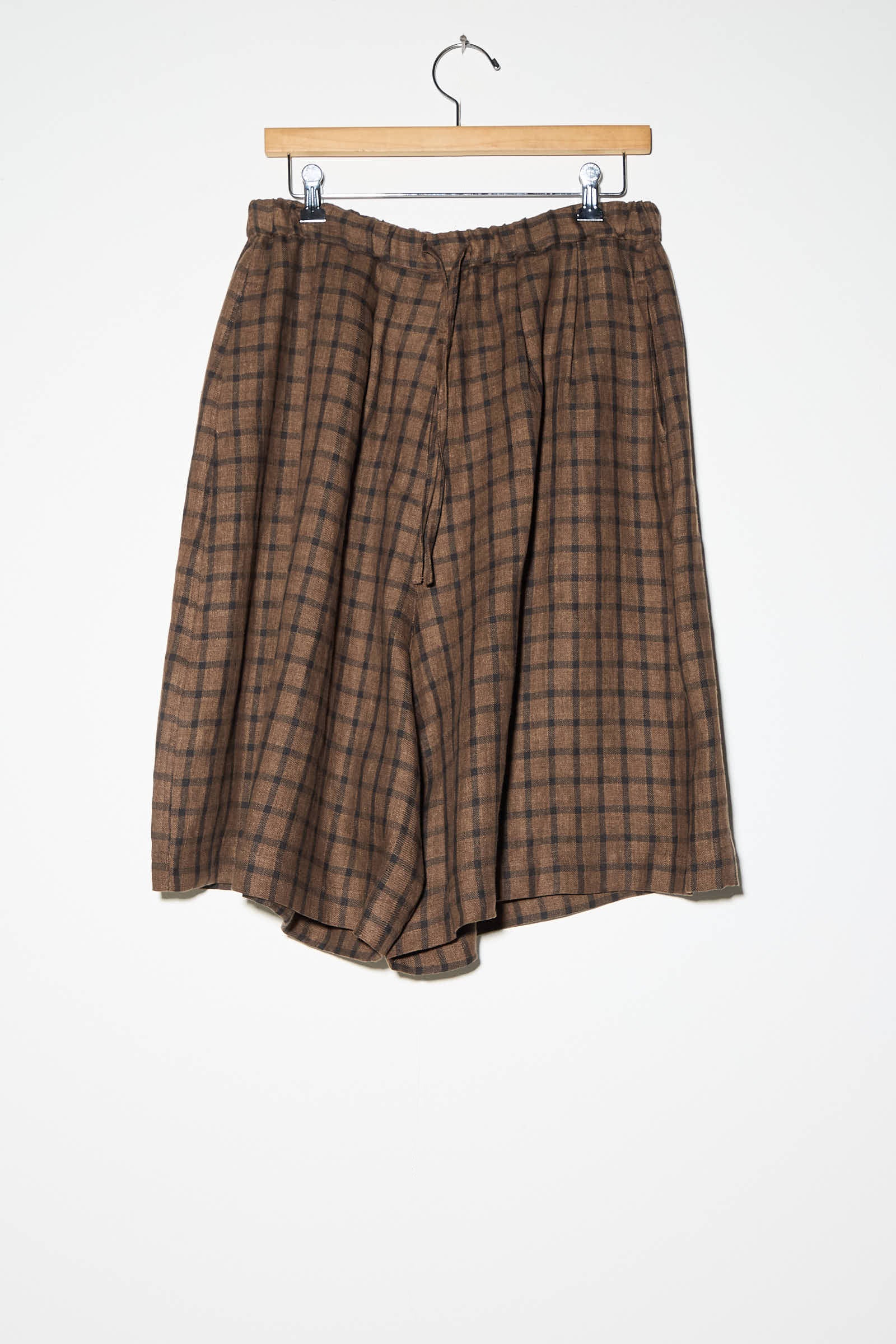 Linen Bermuda Short in Checkered by Cordera hanging on a wooden clothes hanger against a white background.