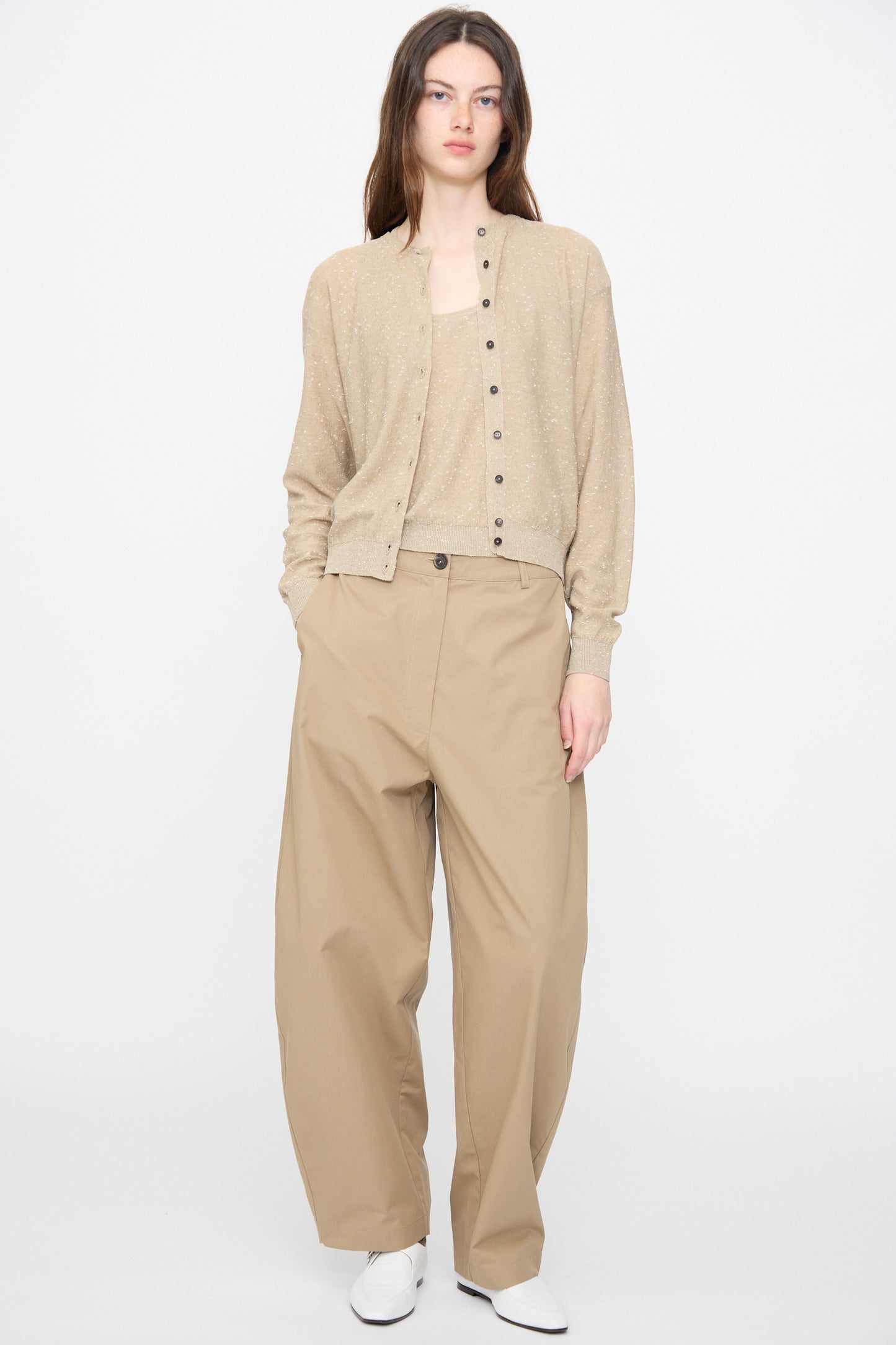Person stands against a plain background wearing the Cordera Linen and Cotton Flecked Cardigan in Taupe, matching top, wide-leg tan trousers, and white shoes, with hands in pockets.