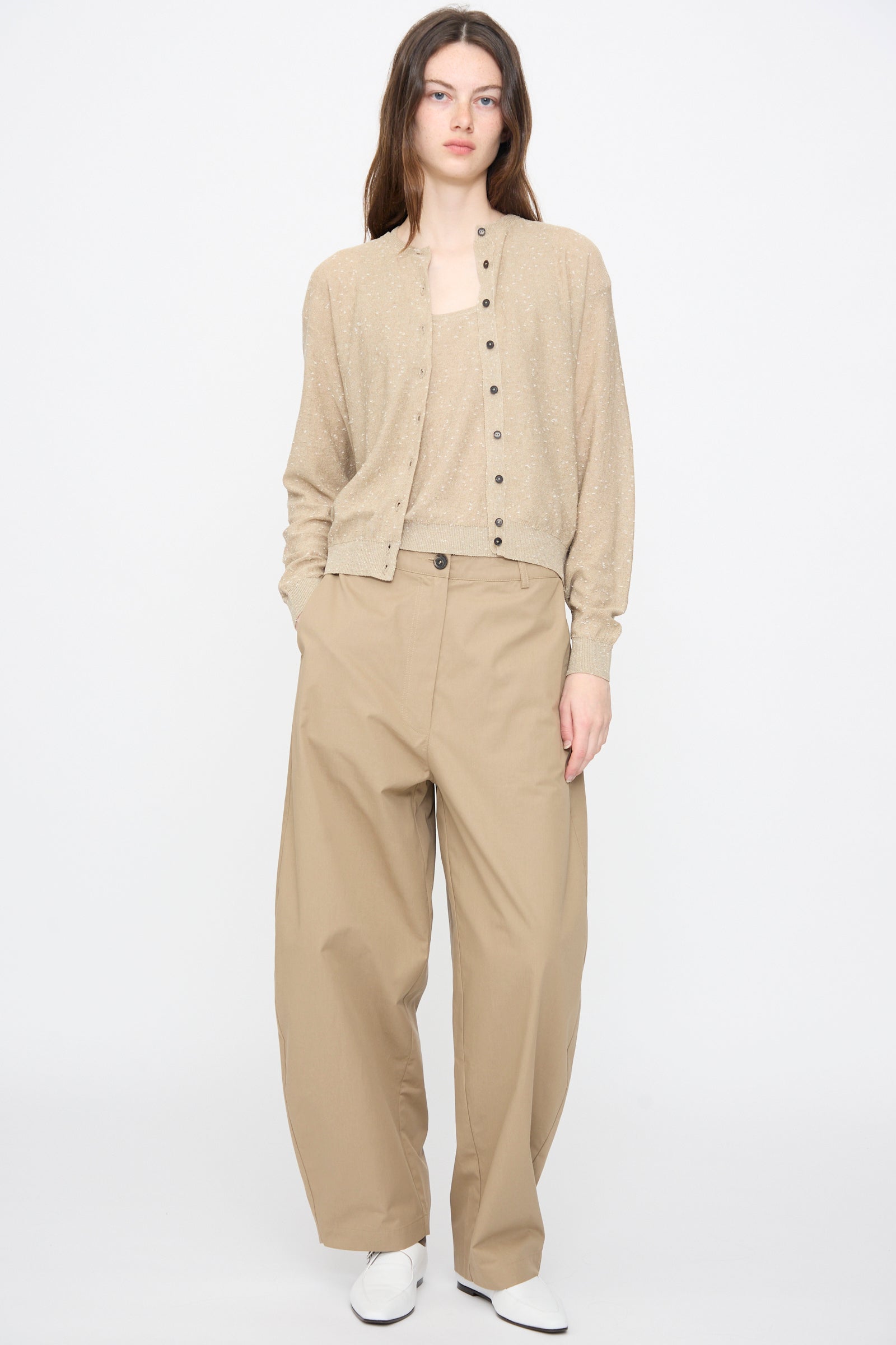 Person stands against a plain background wearing the Cordera Linen and Cotton Flecked Cardigan in Taupe, matching top, wide-leg tan trousers, and white shoes, with hands in pockets.