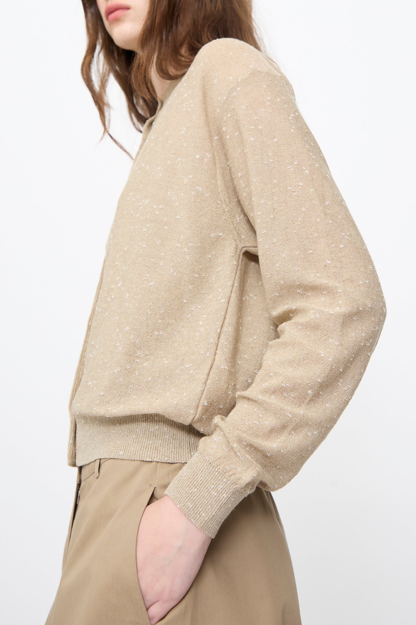 A person wears the Cordera Linen and Cotton Flecked Cardigan in Taupe, featuring subtle white speckles, paired with tan trousers against a plain white background.