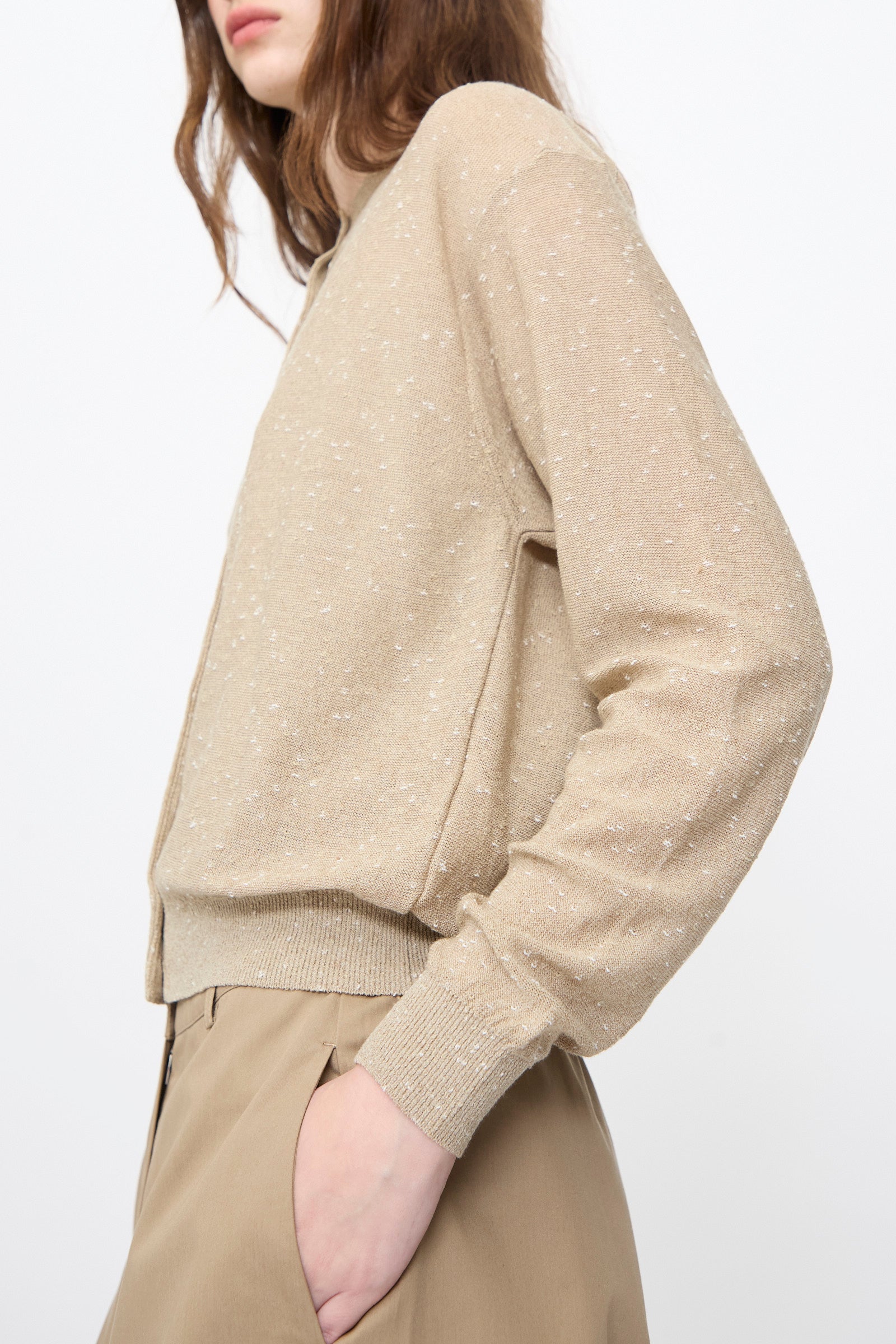 A person wears the Cordera Linen and Cotton Flecked Cardigan in Taupe, featuring subtle white speckles, paired with tan trousers against a plain white background.