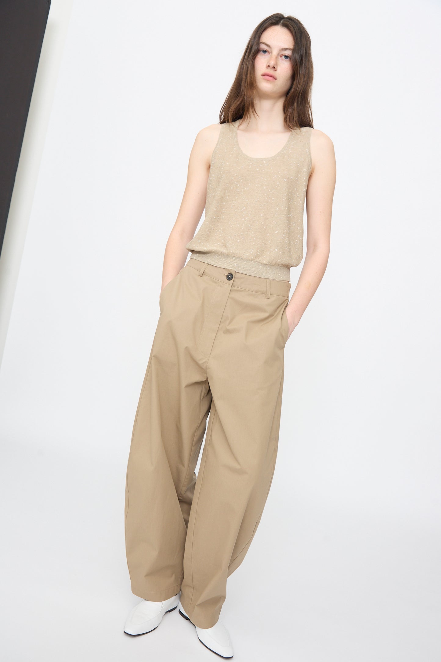 A person stands against a plain background, wearing Cordera’s Linen and Cotton Flecked Tank Top in Beige, paired with wide-legged khaki pants and white shoes, hands tucked casually in pockets.