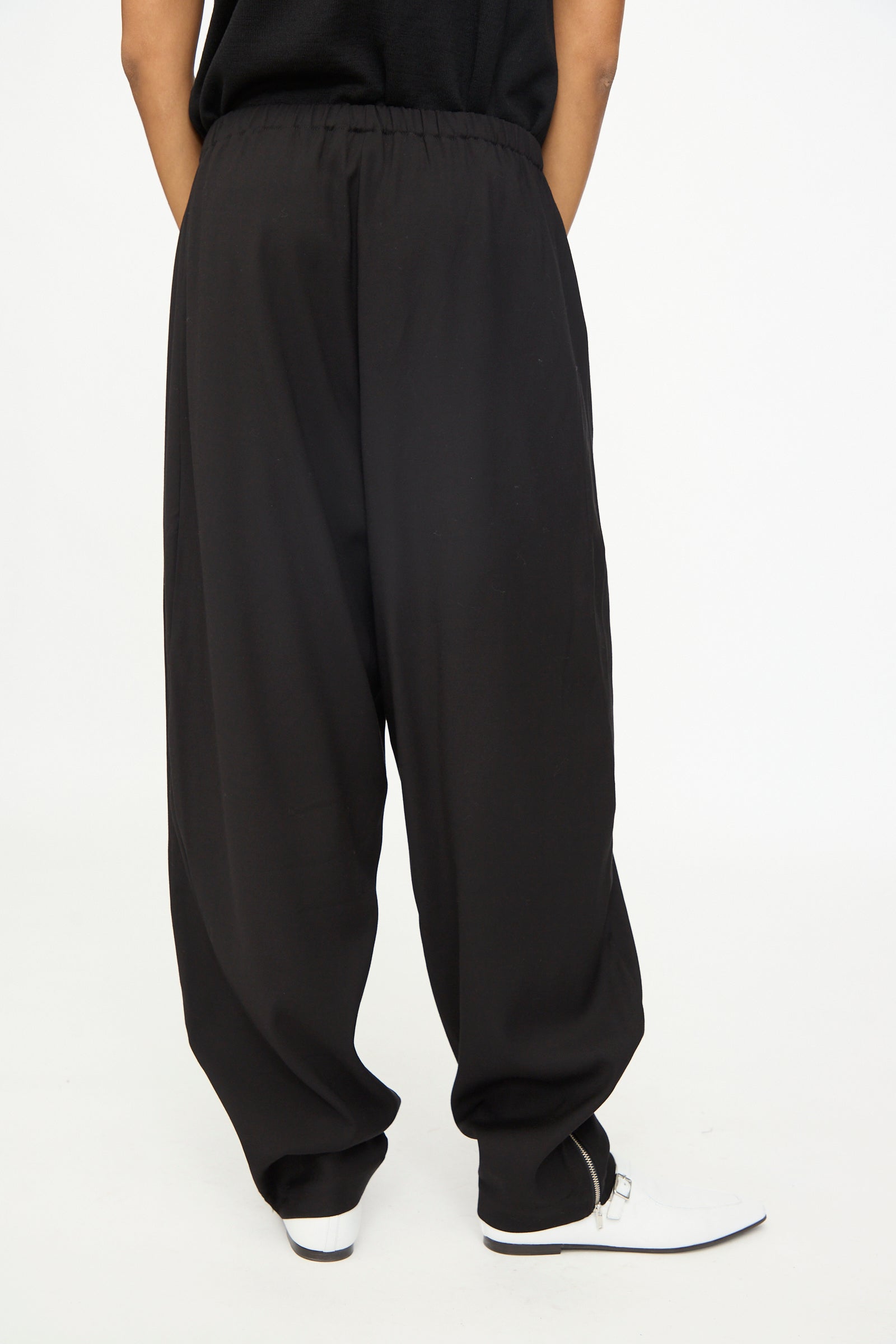 A person is shown wearing the Cordera Lounge Pants in Black, featuring a loose fit and elastic waistband, paired with white shoes and standing with hands behind their back against a plain white background.