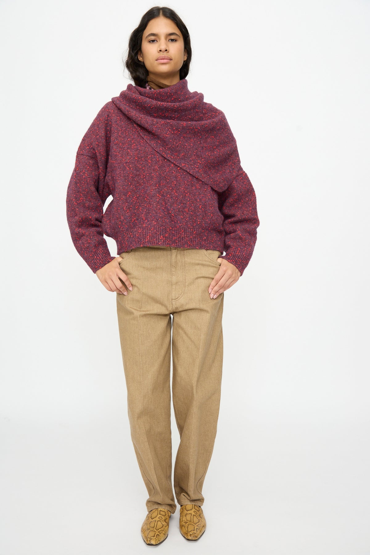 A person wearing a large, textured maroon Maxi Bandana in Beaujolais over a matching speckled sweater, tan trousers, and snakeskin-patterned loafers.
