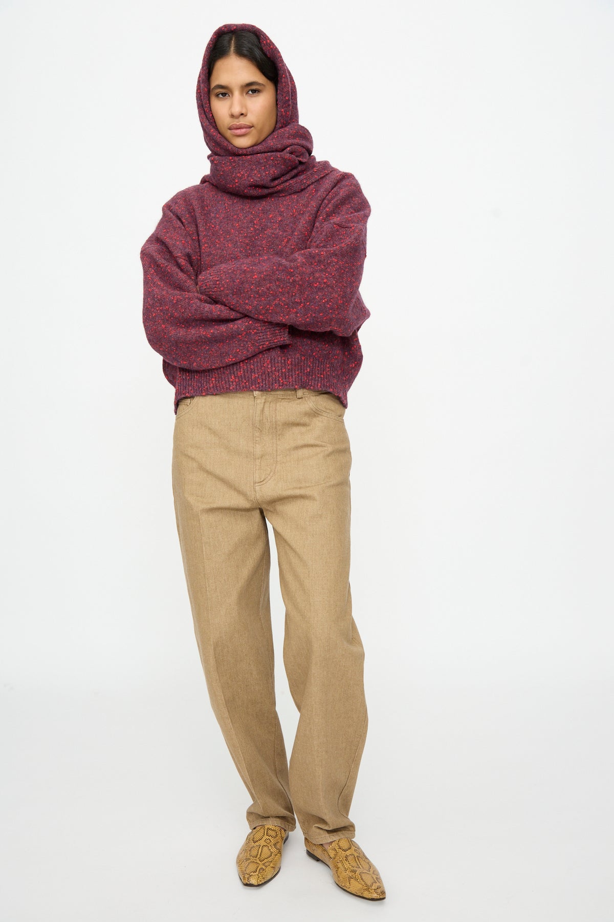 A person wearing a deep red speckled Maxi Bandana in Beaujolais over a matching sweater and khaki trousers.