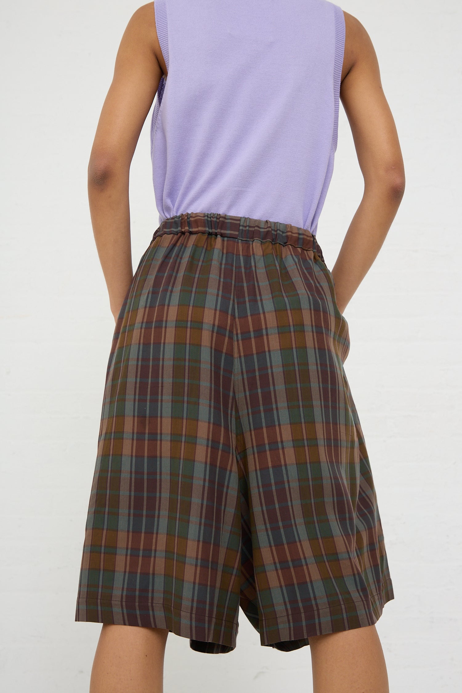 A person standing with their back towards the camera, wearing a purple sleeveless top made from ethically manufactured Tencel and Cordera's Maxi Bermuda Short in Checkered.