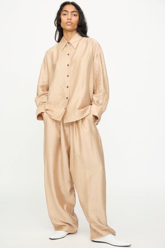 A person wearing Cordera's Maxi Pants in Beige, styled with an oversized beige button-up shirt and white shoes, stands against a plain white background.