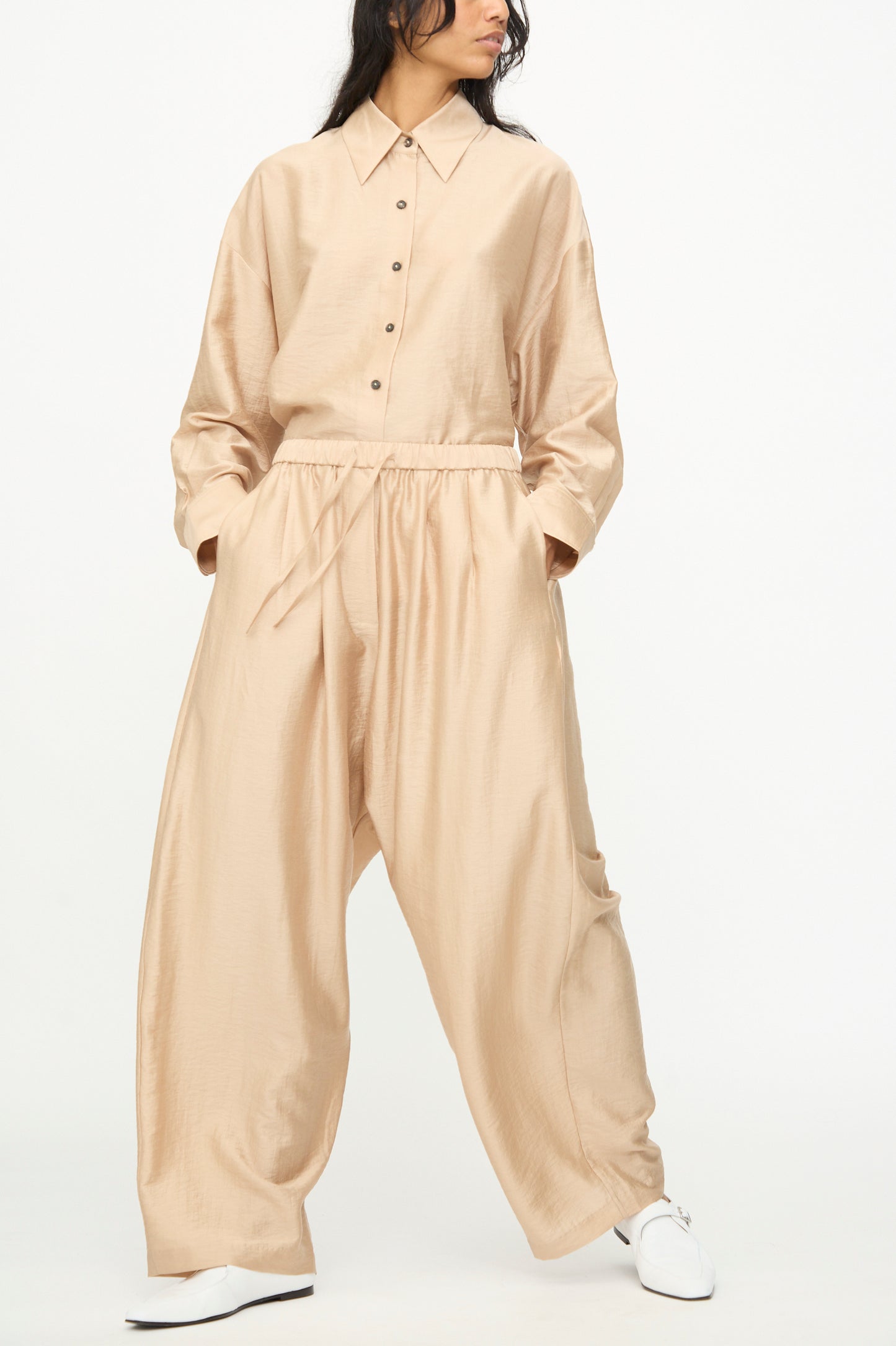 A person wearing Cordera's Maxi Pants in Beige—wide leg and oversized, crafted from a soft lyocell blend—stands with hands in pockets against a plain white background.