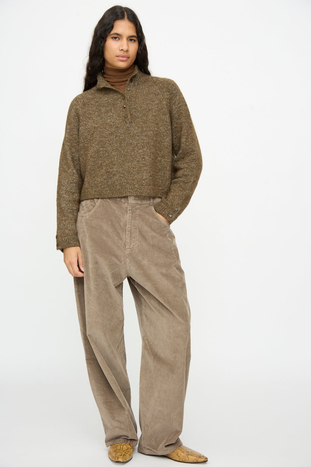 A person wears a brown Melange Polo Sweater in Pardo over a brown turtleneck with wide-leg trousers.