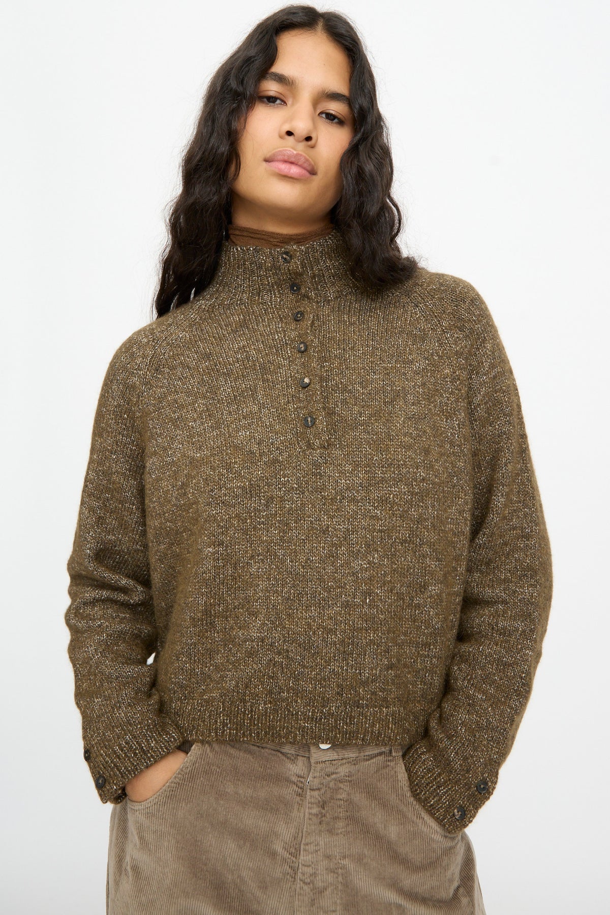 A person wearing a Cordera Melange Polo Sweater in Pardo, a brown, speckled cropped knit sweater with a buttoned polo neck.