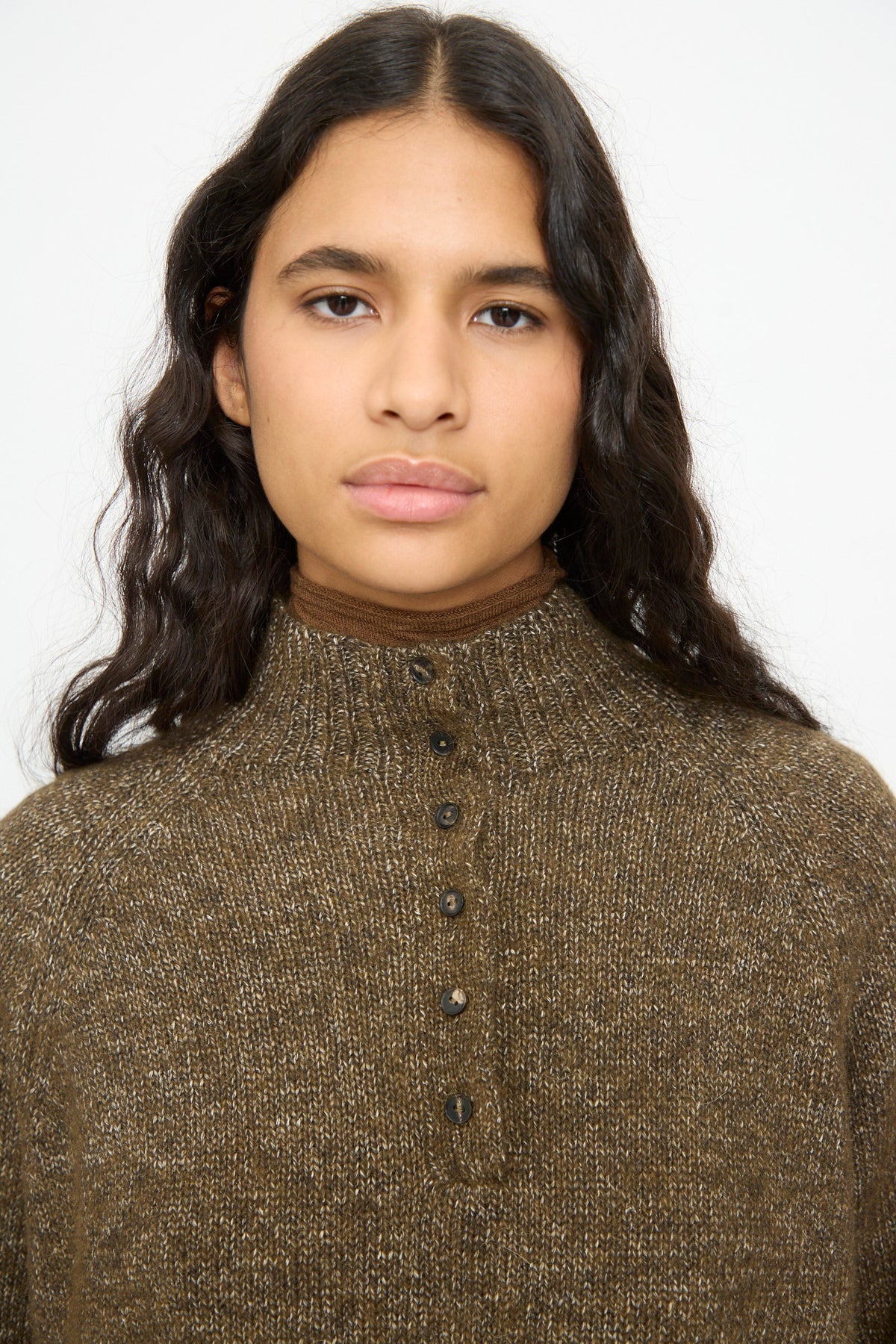A person wears a brown, speckled knit cotton blend Melange Polo Sweater in Pardo with a buttoned polo neck over a brown high-neck undershirt.