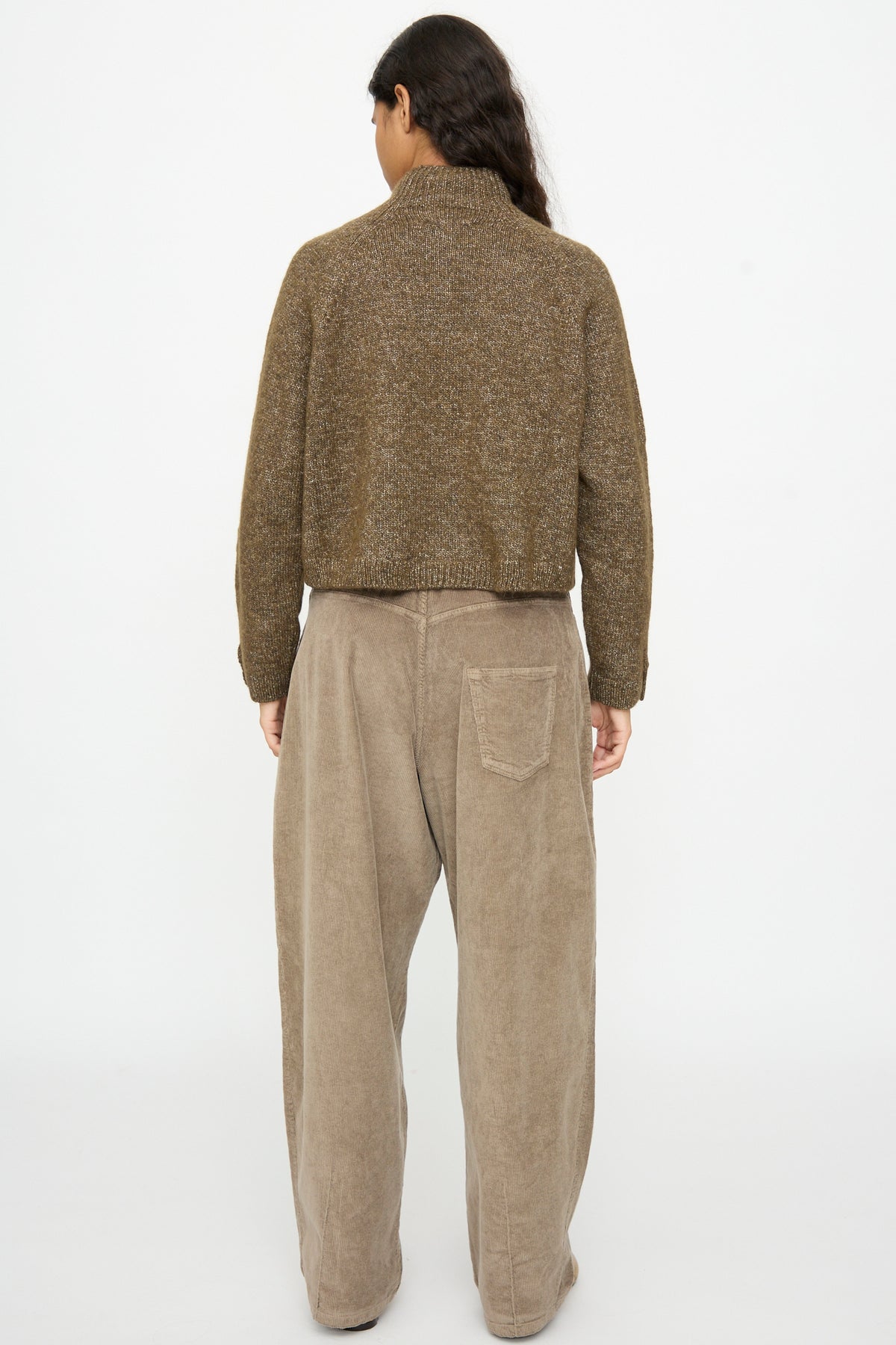 Back view of a person wearing a brown Melange Polo Sweater in Pardo and loose-fitting tan trousers.