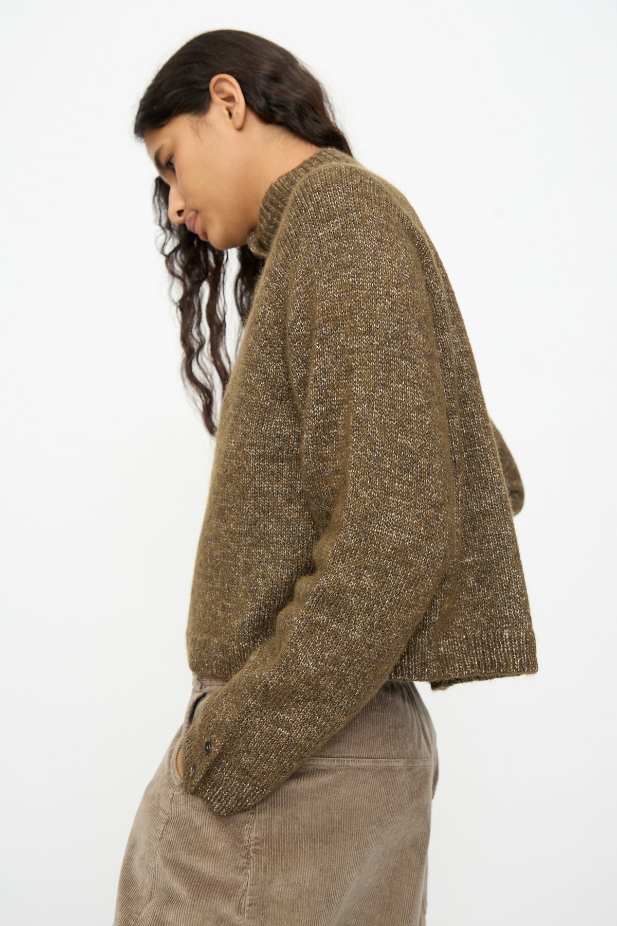Person wearing a speckled olive green Melange Polo Sweater in Pardo with a buttoned polo neck and tan corduroy pants.