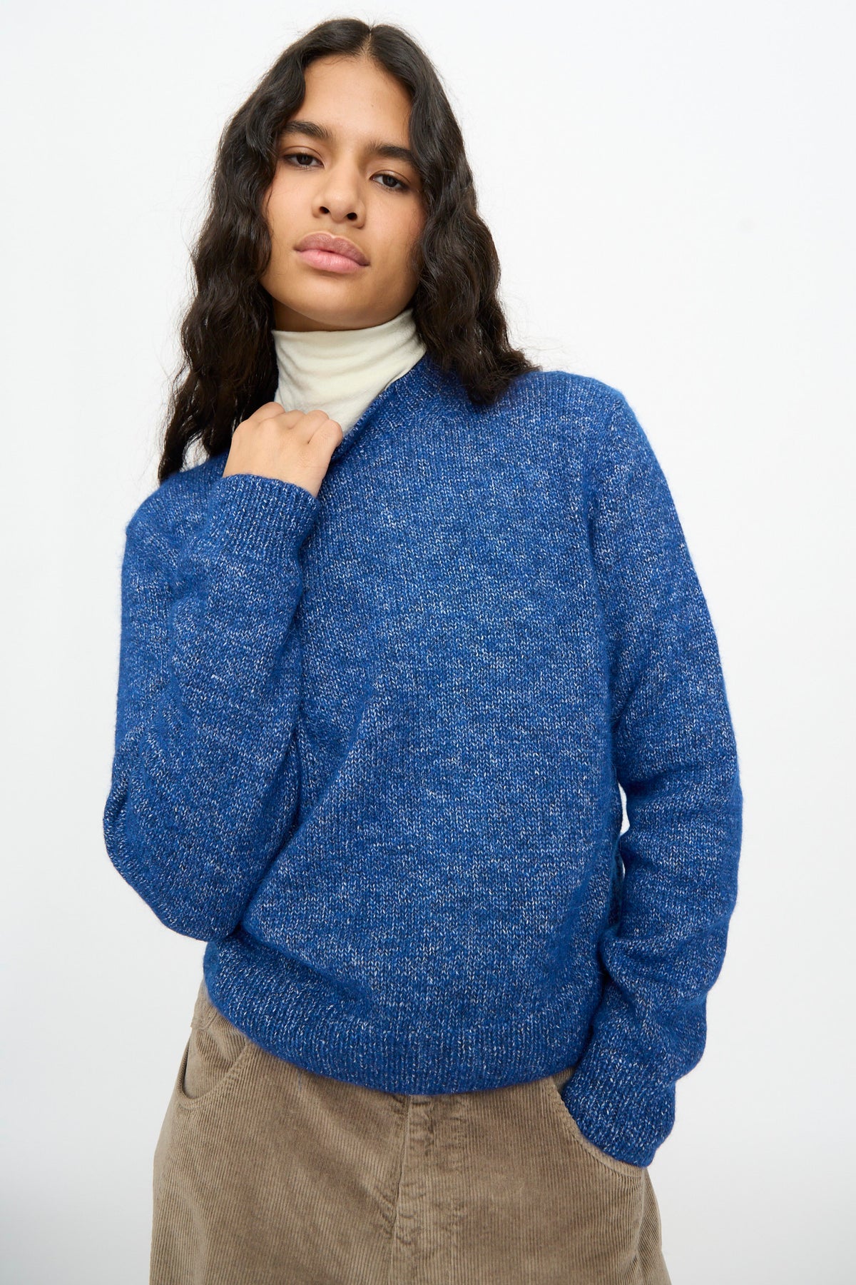 Person wearing a relaxed fit blue Melange Sweater over a cream turtleneck and tan pants.