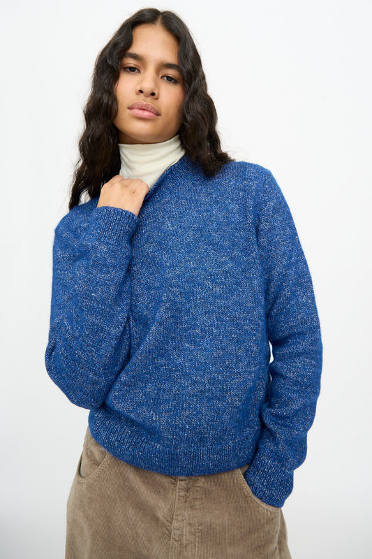 Person wearing a relaxed fit blue Melange Sweater over a cream turtleneck and tan pants.