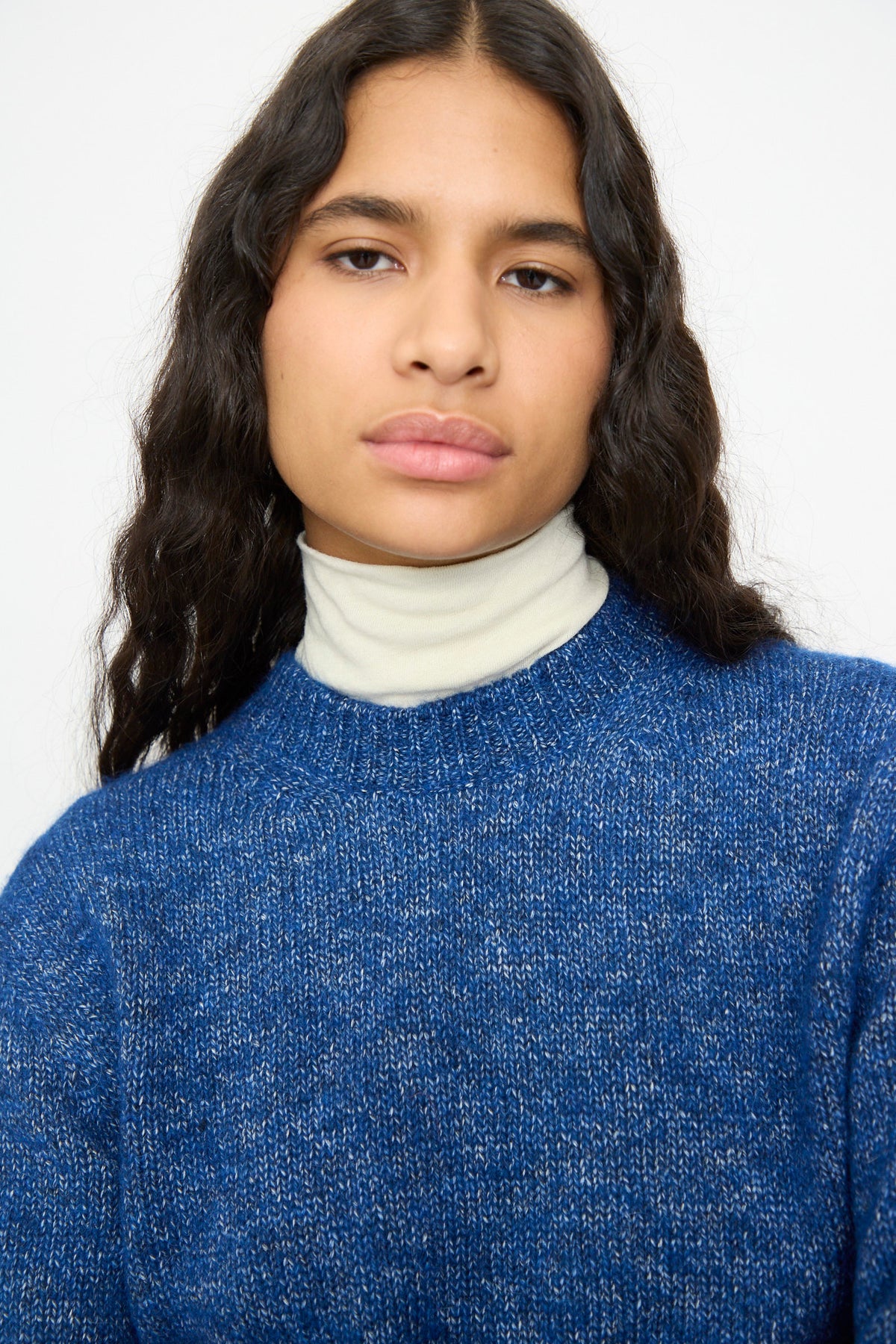 A relaxed fit Cordera Melange Sweater in Blue layered over a cream turtleneck.