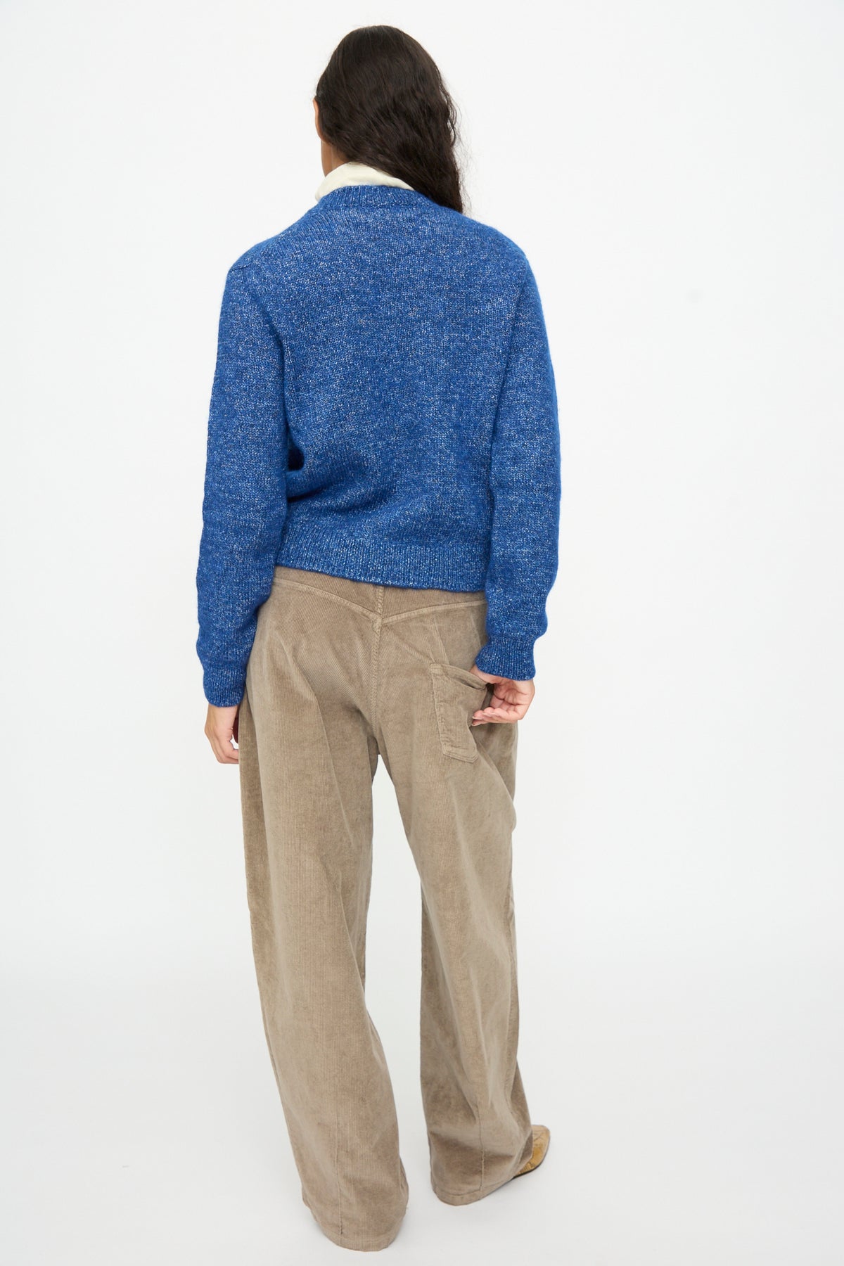A person seen from behind, wearing a blue, relaxed fit Cordera Melange Sweater in Blue and tan corduroy pants.