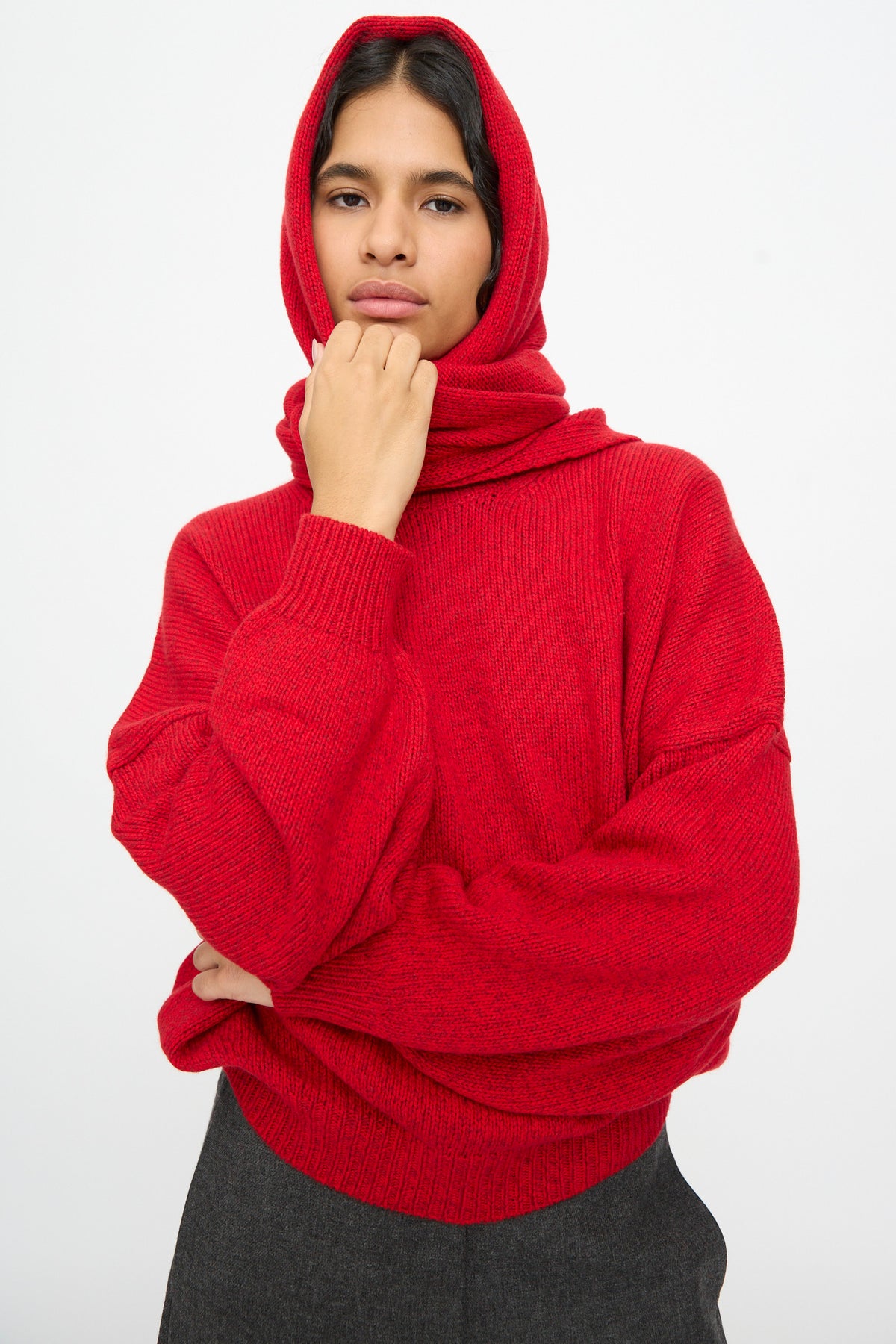 A person wearing a bright red knit hooded sweater with the hood pulled up, paired with a Cordera Merino and Cashmere Maxi Bandana in Red.