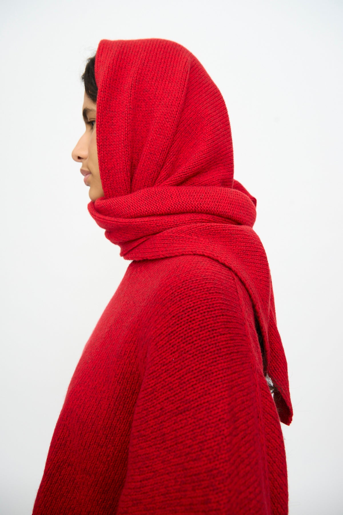 Profile view of a person wearing a red Merino and Cashmere Maxi Bandana in a large triangular shape over a matching red sweater.