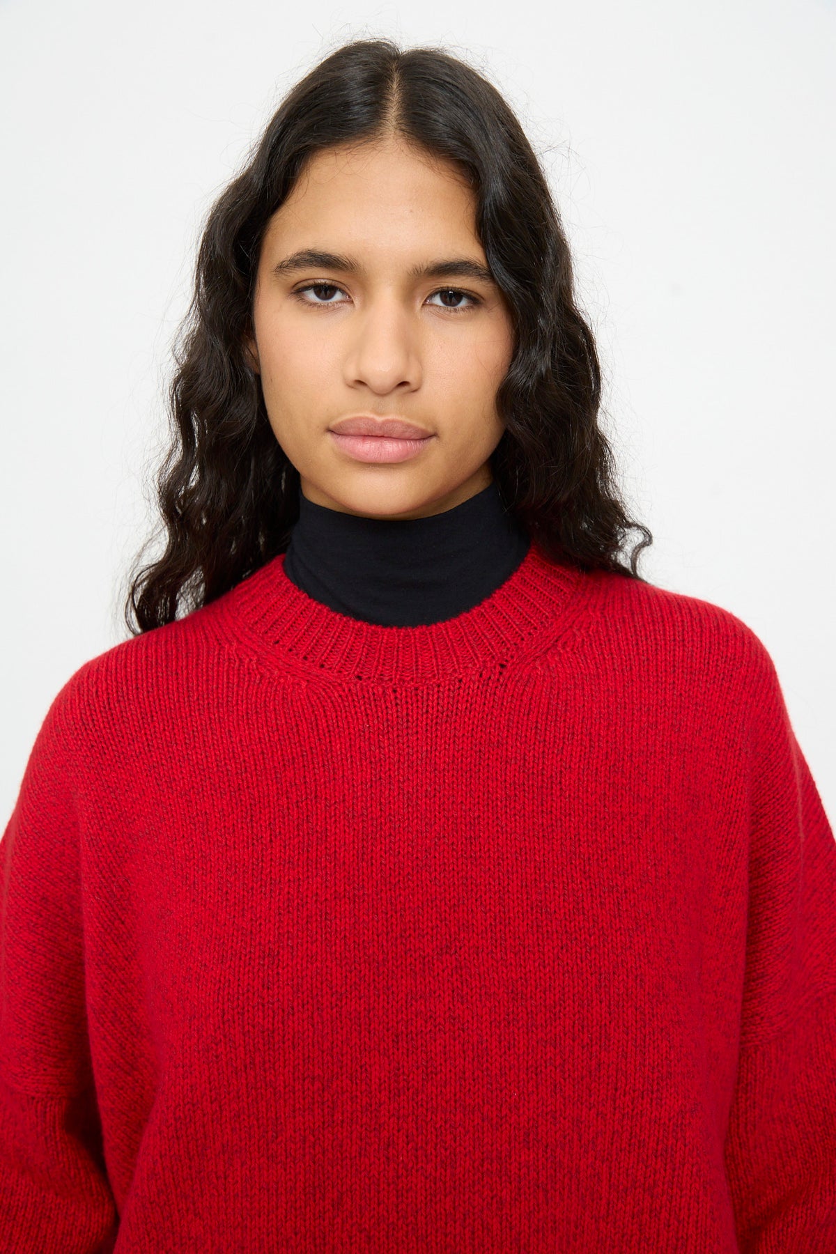 A person wearing a Cordera Merino and Cashmere Sweater in red over a black mock-neck top.