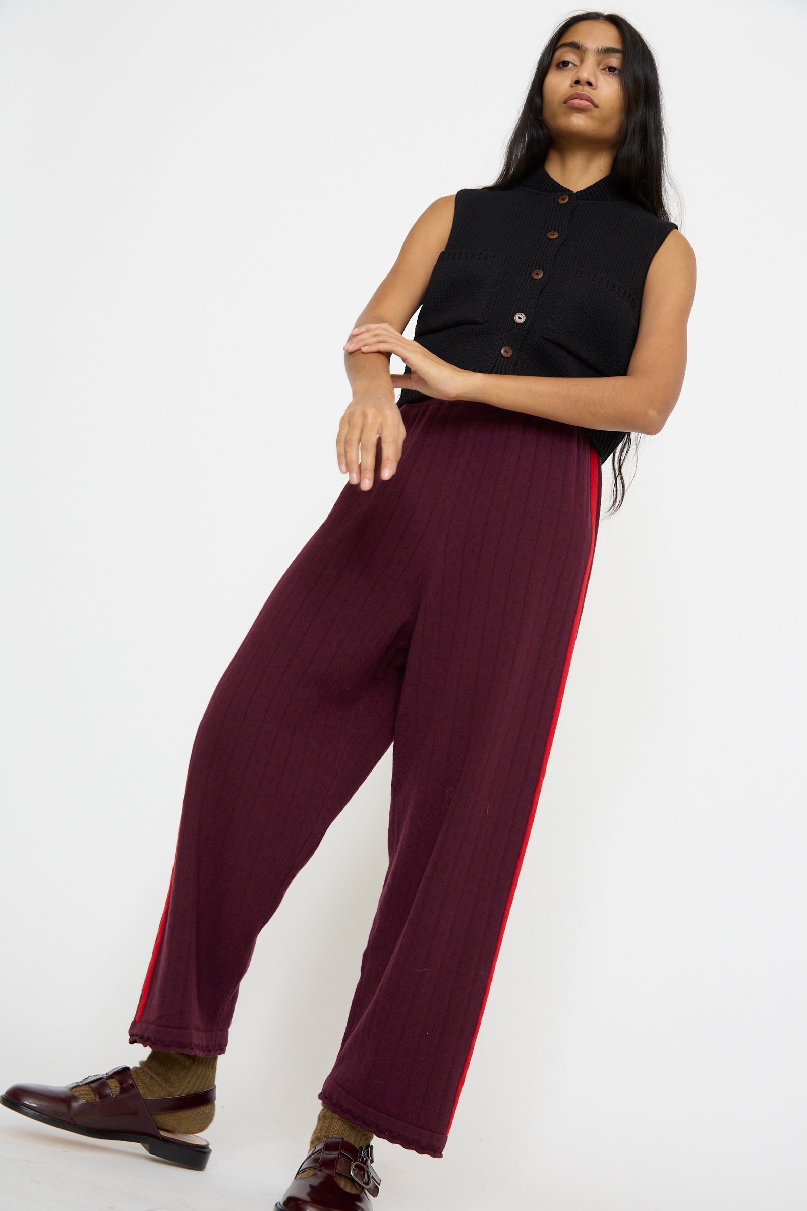 The model poses gainst a plain background wearing Cordera's Merino Perlé Pant in Burgundy and a black sleeveless top.