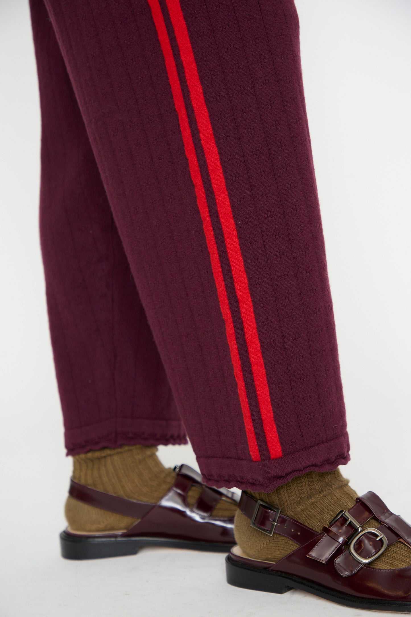 A person wearing Cordera's Merino Perlé Pant in Burgundy, paired with cozy brown socks and brown sandals. Close up of ankle. 