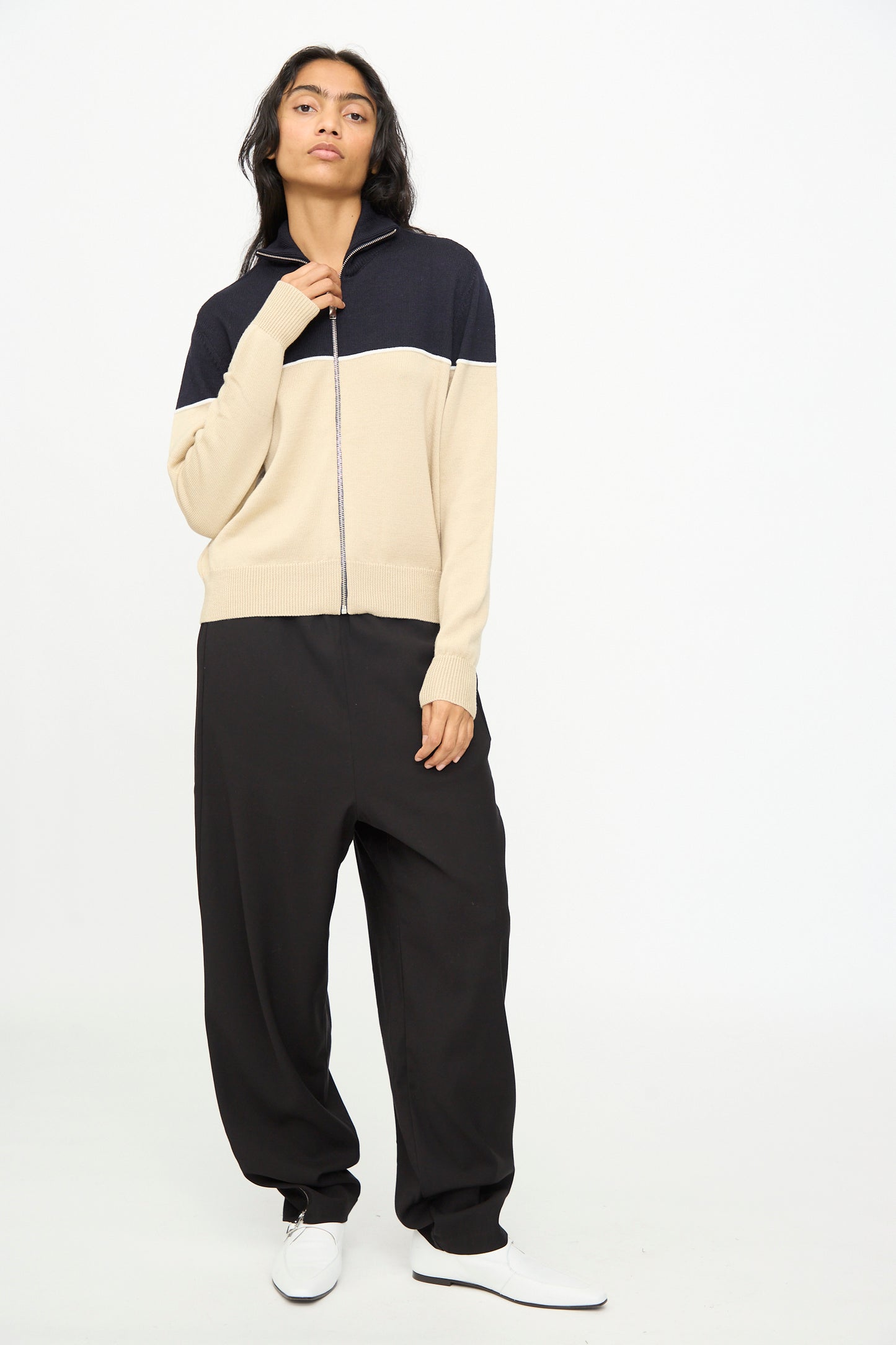 A person stands against a plain background, wearing the Cordera Merino Wool Cardigan in Colorblock, styled with loose black pants and white shoes.