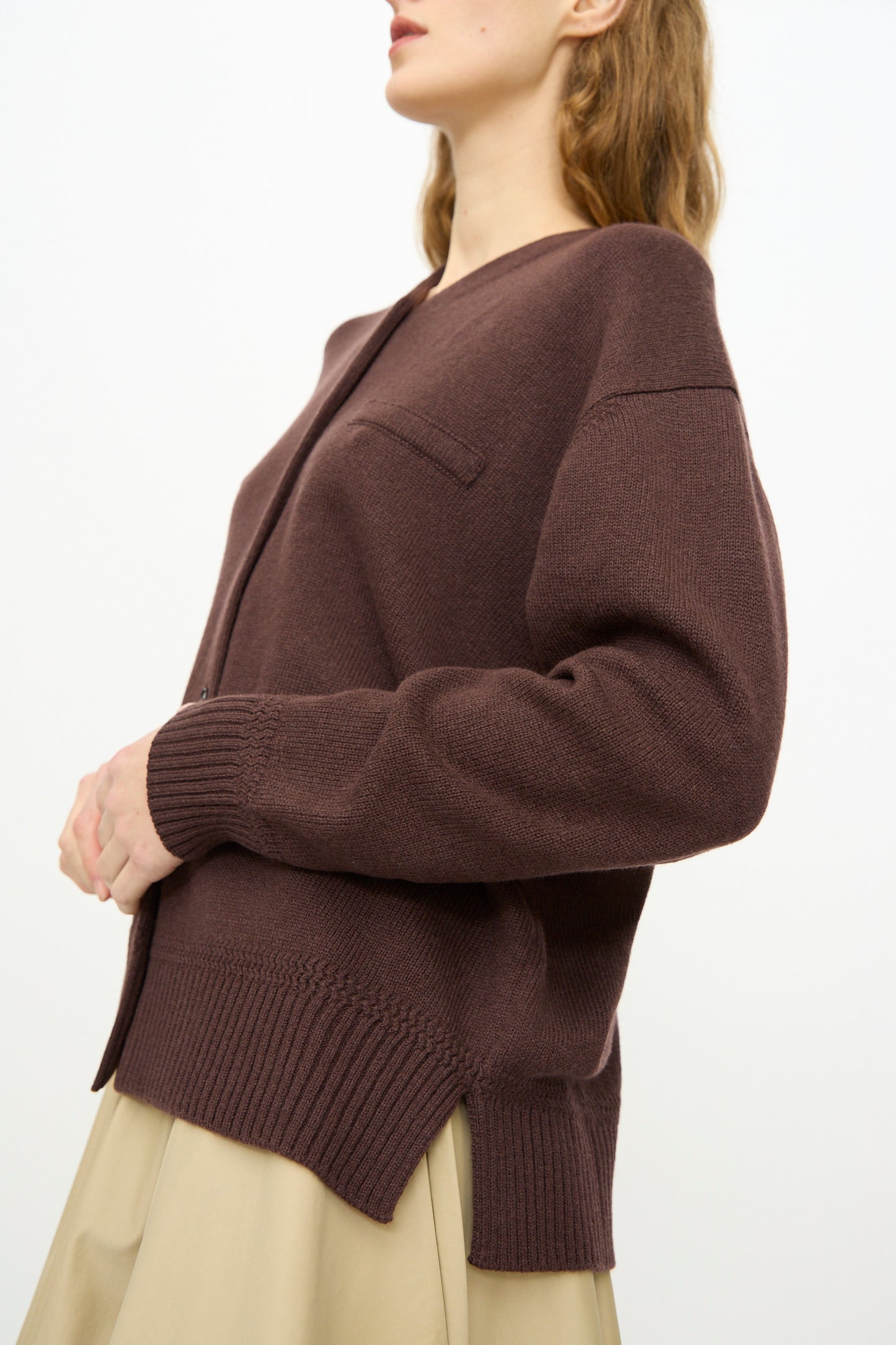 A person wearing the Cordera Merino Wool Cardigan in Prune, shown from the side against a plain background, paired with a beige skirt.