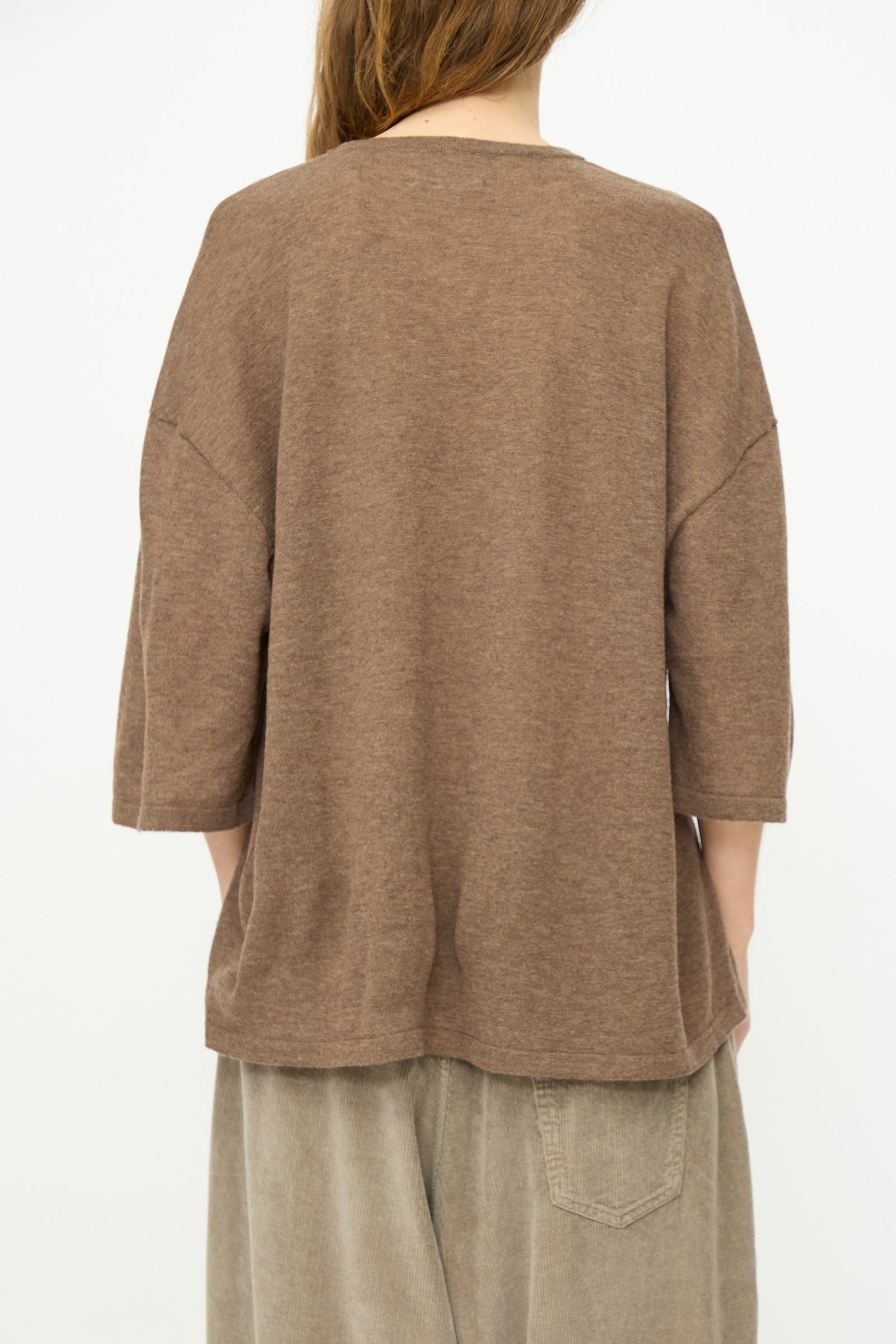 A person stands with their back to the camera, wearing Cordera's Merino Wool Oversized T-Shirt in Deep Taupe and beige pants against a plain light background.
