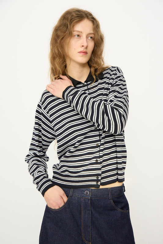 A person with wavy hair wears the Cordera Merino Wool Polo Cardigan in Striped with a dark denim skirt, standing against a plain light background and looking to the side.