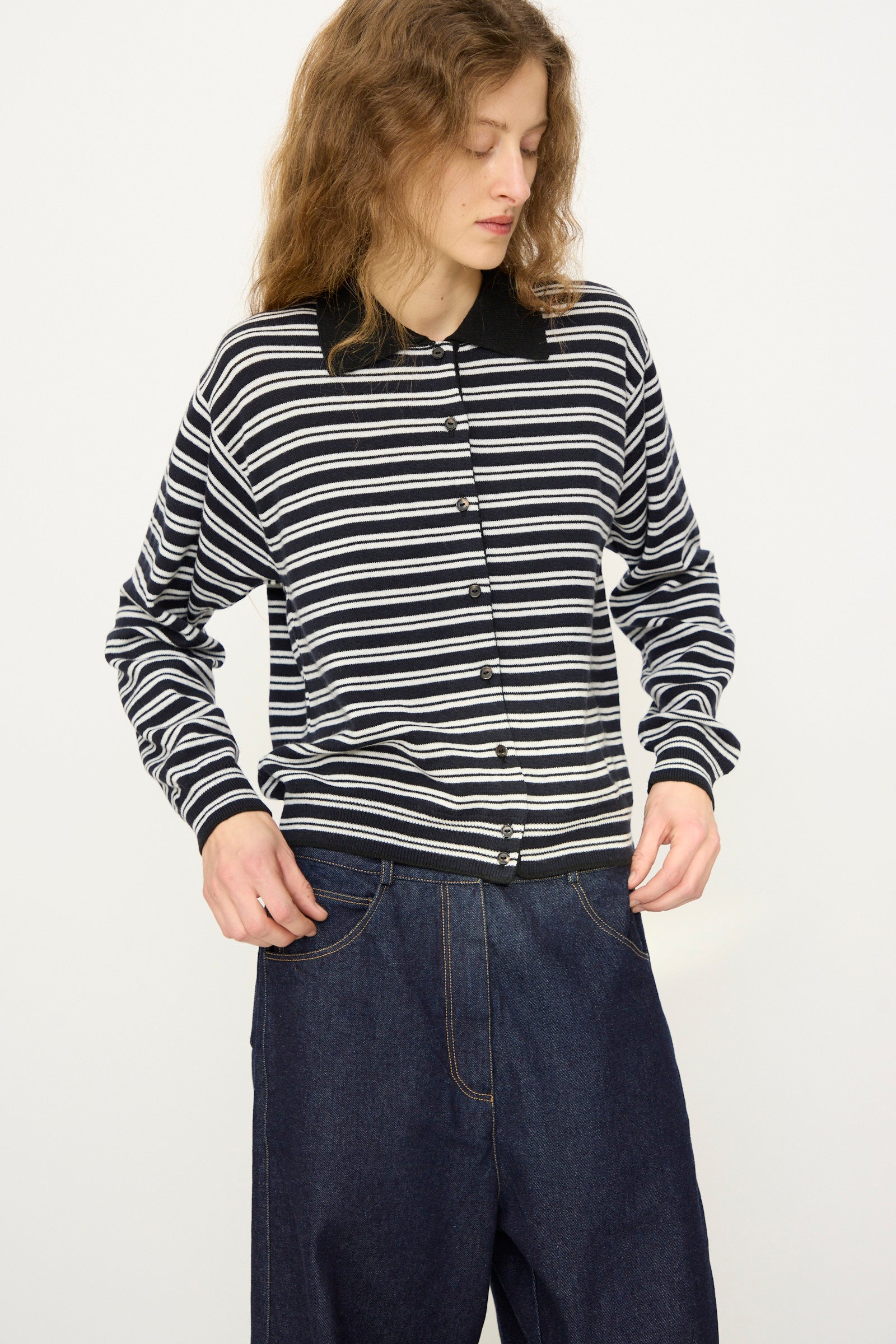 A person wearing Cordera's Merino Wool Polo Cardigan in Striped stands against a plain light background, styled with loose-fitting dark blue jeans.